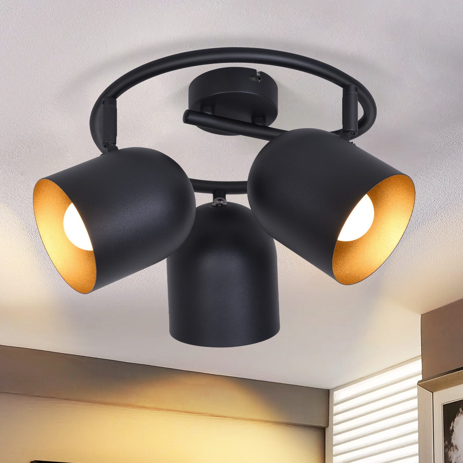Lampada da soffitto nera con tre faretti regolabili, interno dorato. Soffitto bianco.
