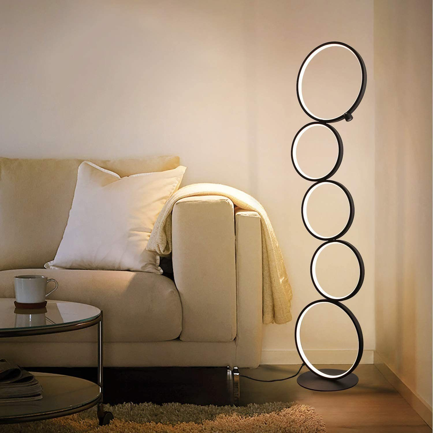 Hohe, schwarze Stehlampe mit fünf weißen Lichtkreisen in einem Wohnzimmer.