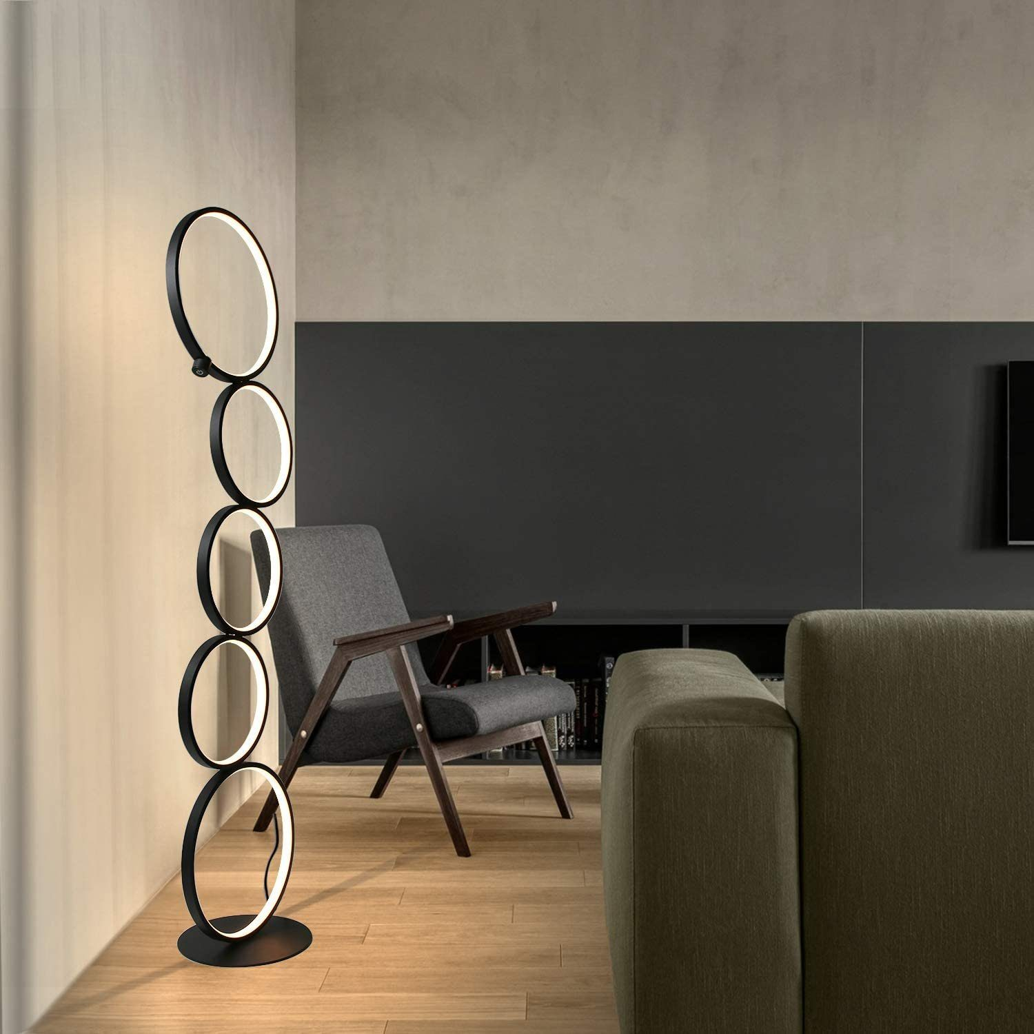Eine hohe schwarze Stehlampe mit fünf kreisförmigen Lichtringen. Ein graues Sofa und eine Wand im Hintergrund.