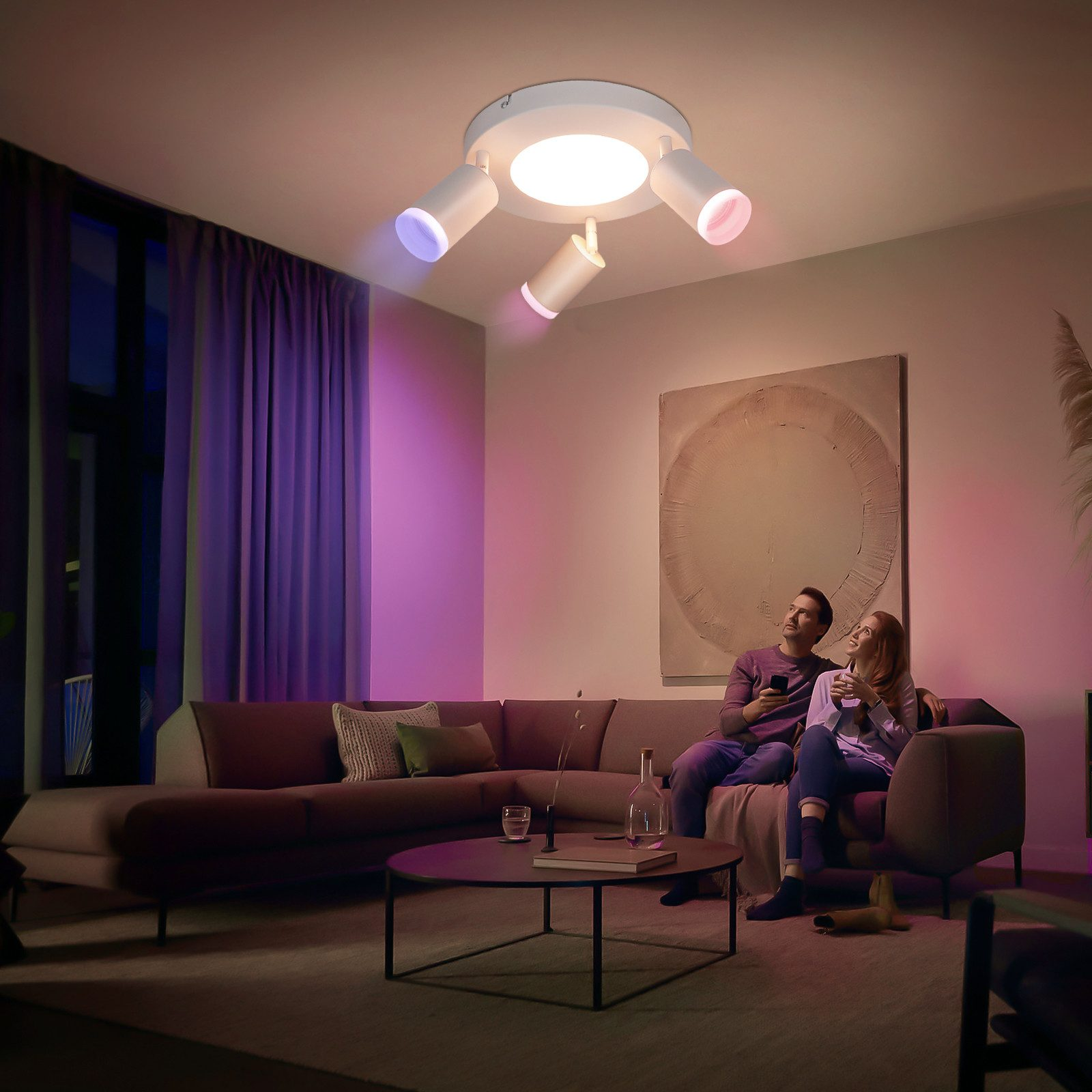 Soggiorno con coppia su divano, illuminato da una luce a soffitto con faretti colorati.