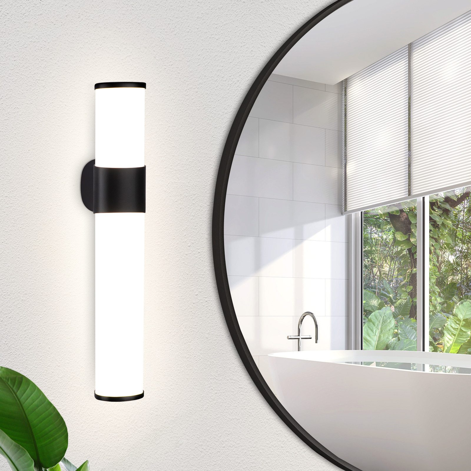 Una lampada da parete con due cilindri bianchi. Uno specchio riflette un bagno con vasca e finestra.