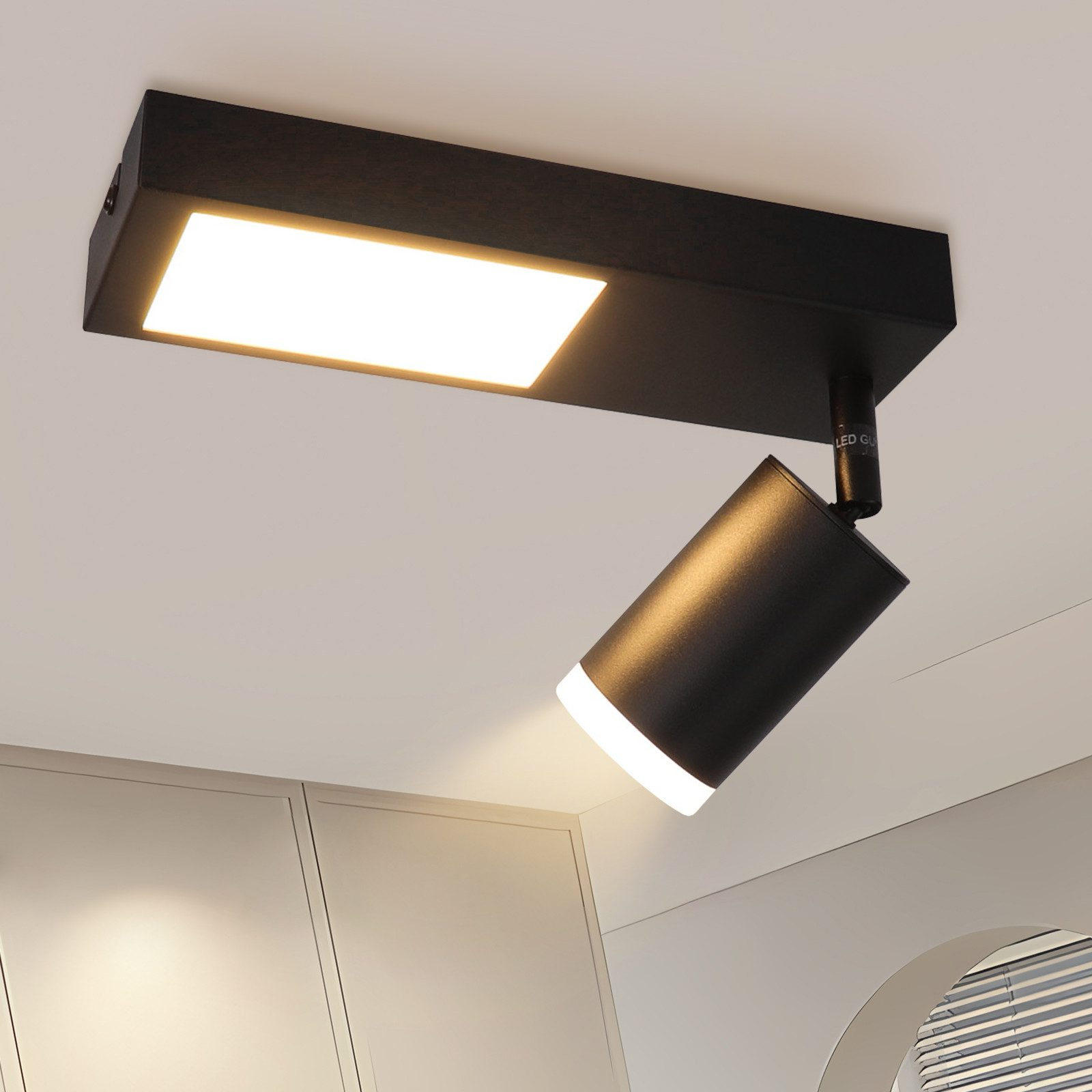 Apparecchio a faretto rettangolare nero montato su un soffitto bianco, con una luce cilindrica girevole.