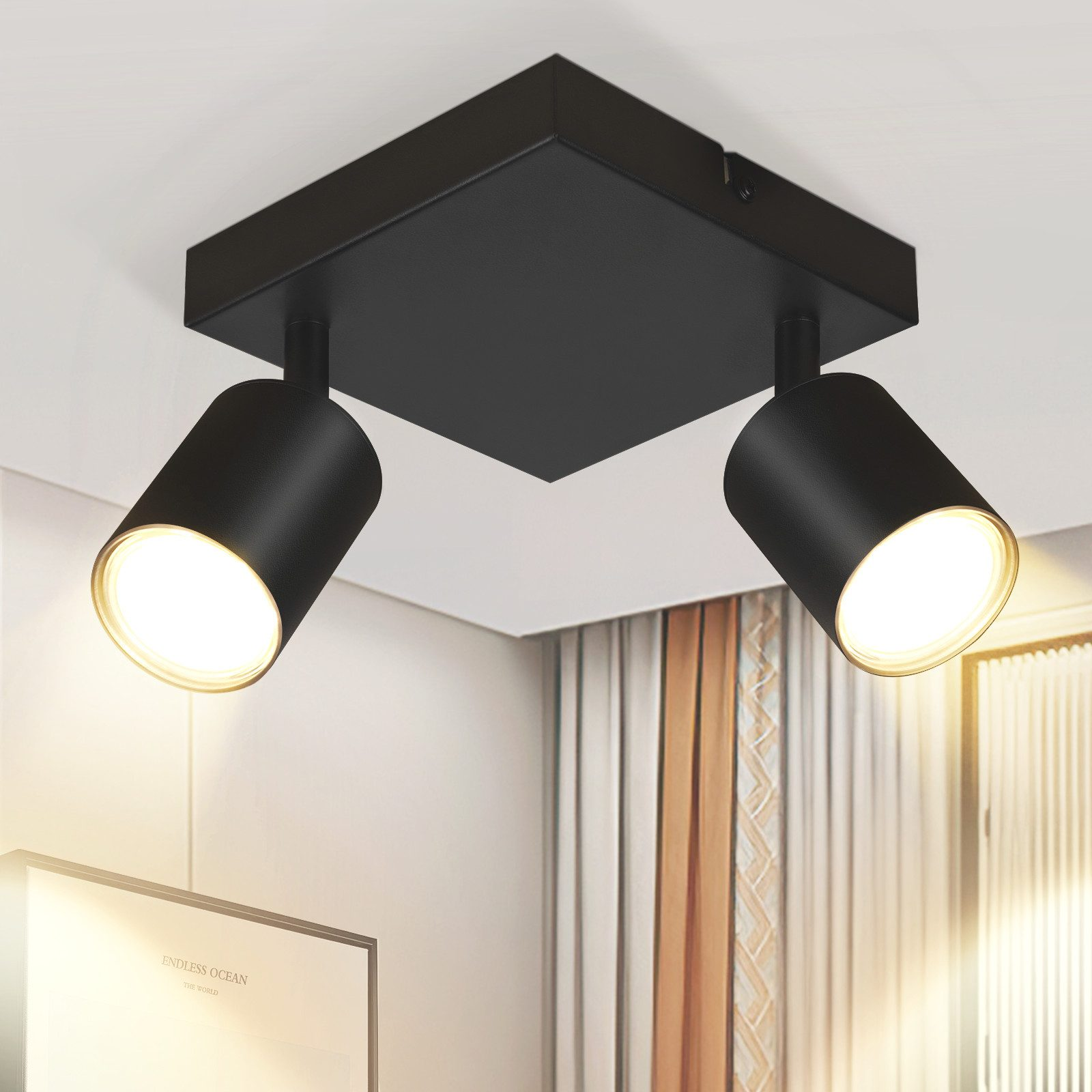 Apparecchio di illuminazione a soffitto con quattro faretti neri. Le luci sono dirette verso il basso, illuminando la stanza.
