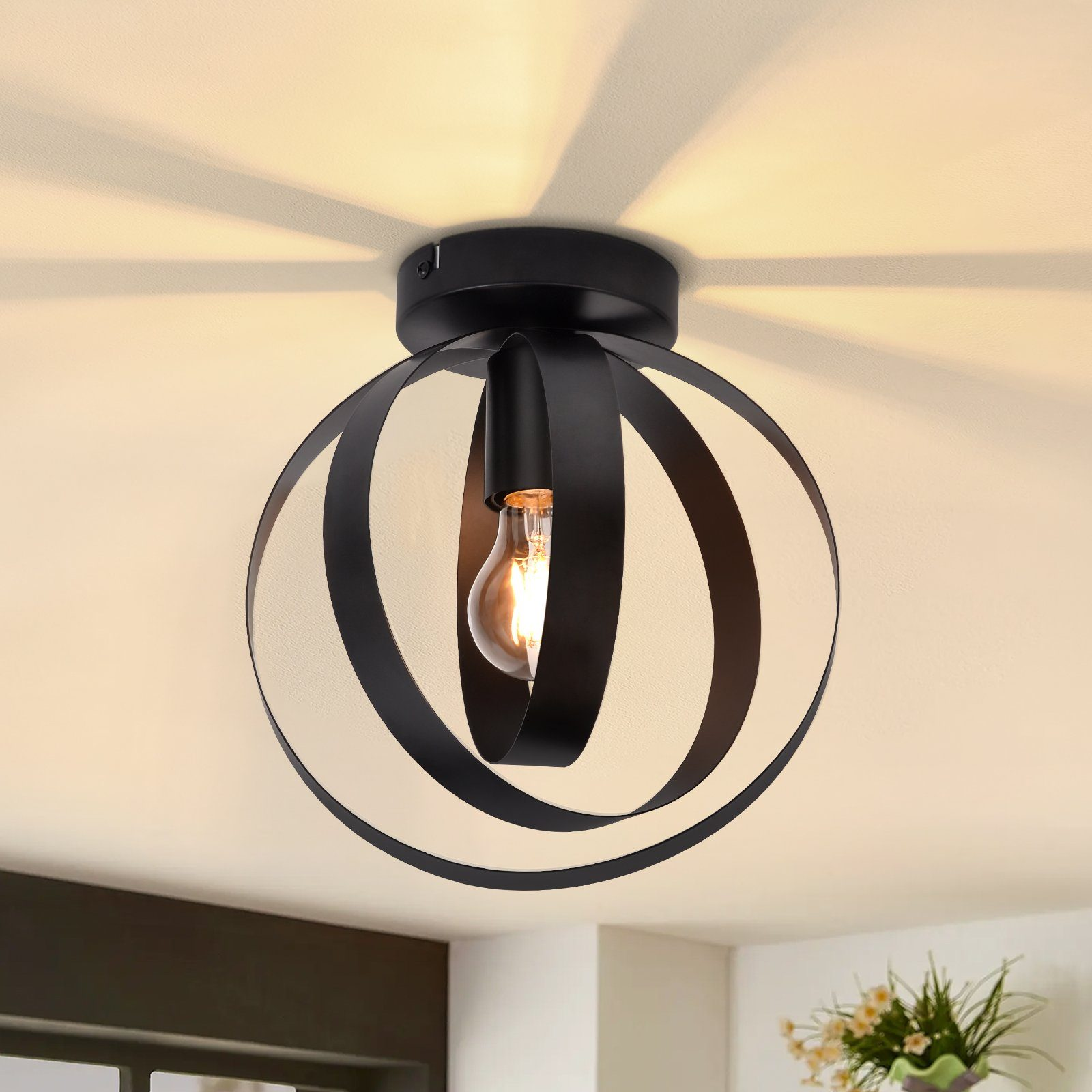 Lampada da soffitto nera a forma di globo con una lampadina visibile. Le ombre sono proiettate sul soffitto.