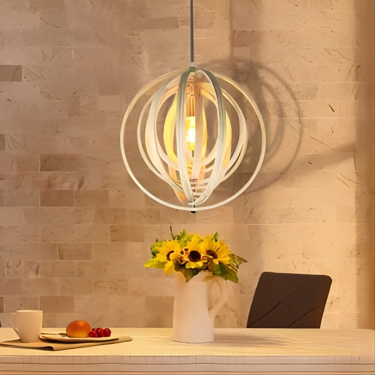 Lampada a sospensione decorativa sopra un tavolo con fiori, frutta e una tazza di caffè.
