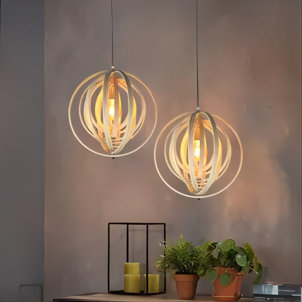 Due lampade a sospensione sferiche in legno, con un telaio in metallo nero e piante sottostanti.