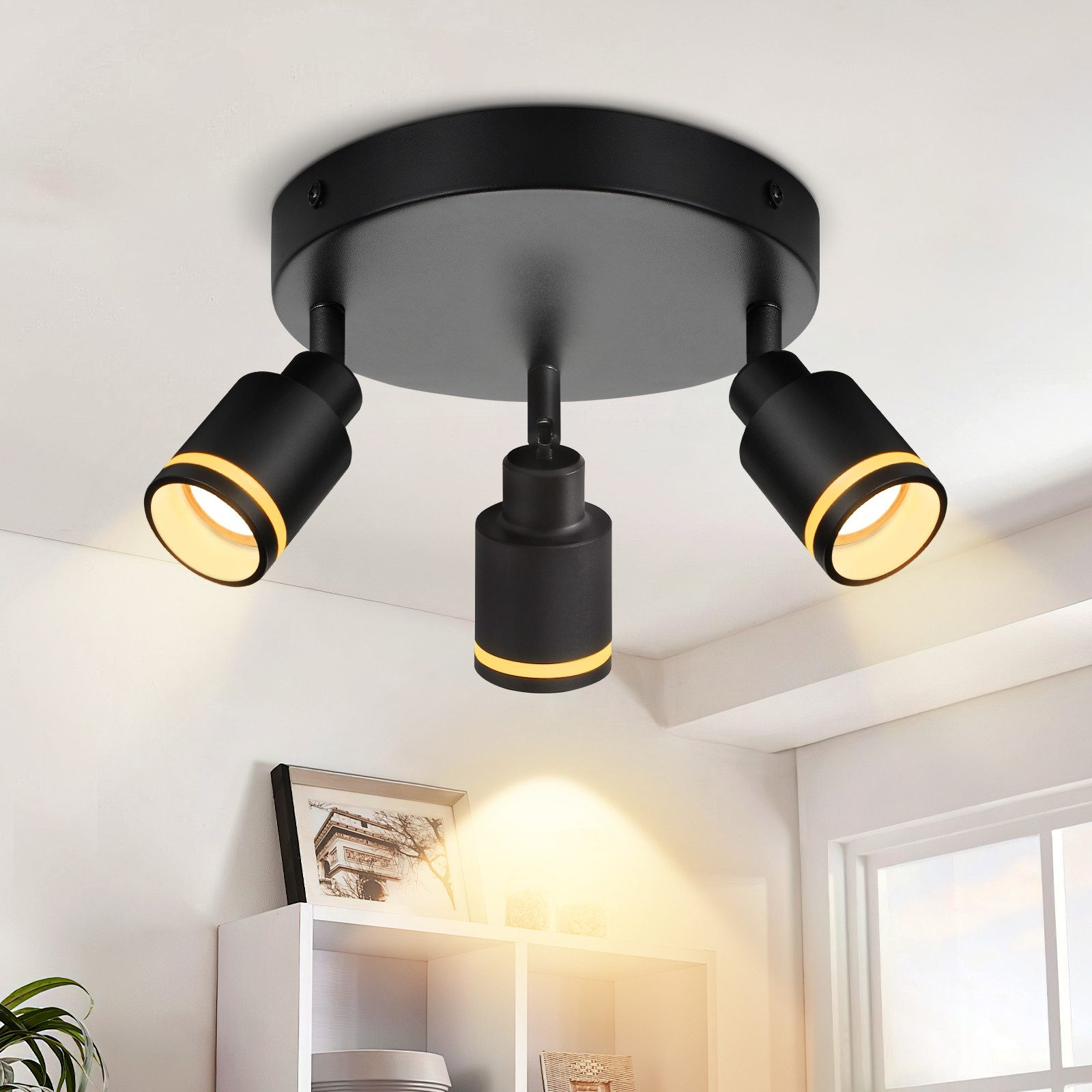 Lampada da soffitto nera con tre faretti, che emettono luce gialla. Lo sfondo è un soffitto bianco.