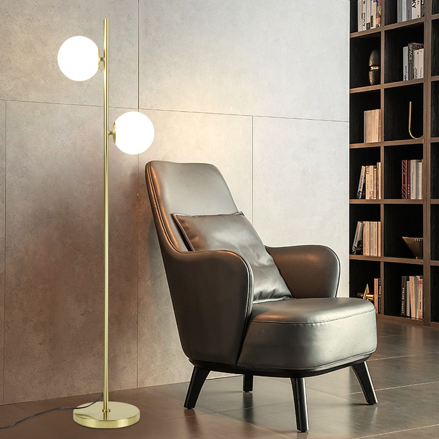 Una lampada da terra dorata con due globi bianchi accanto a una poltrona in pelle.