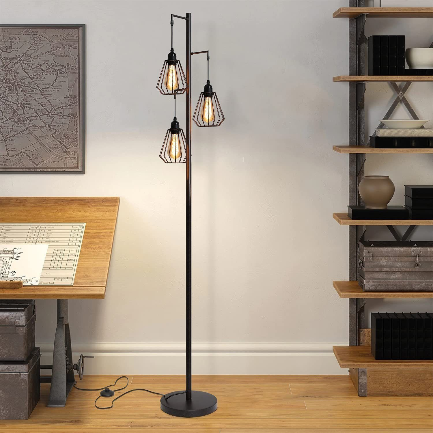 Lampada da terra in metallo nero con tre luci a gabbia sospese. Una scrivania in legno e una libreria sullo sfondo.