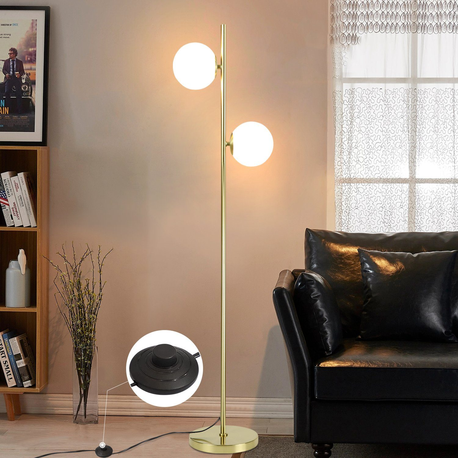 Una lampada da terra dorata con due globi bianchi. Divano nero a destra. Scaffale in legno a sinistra.