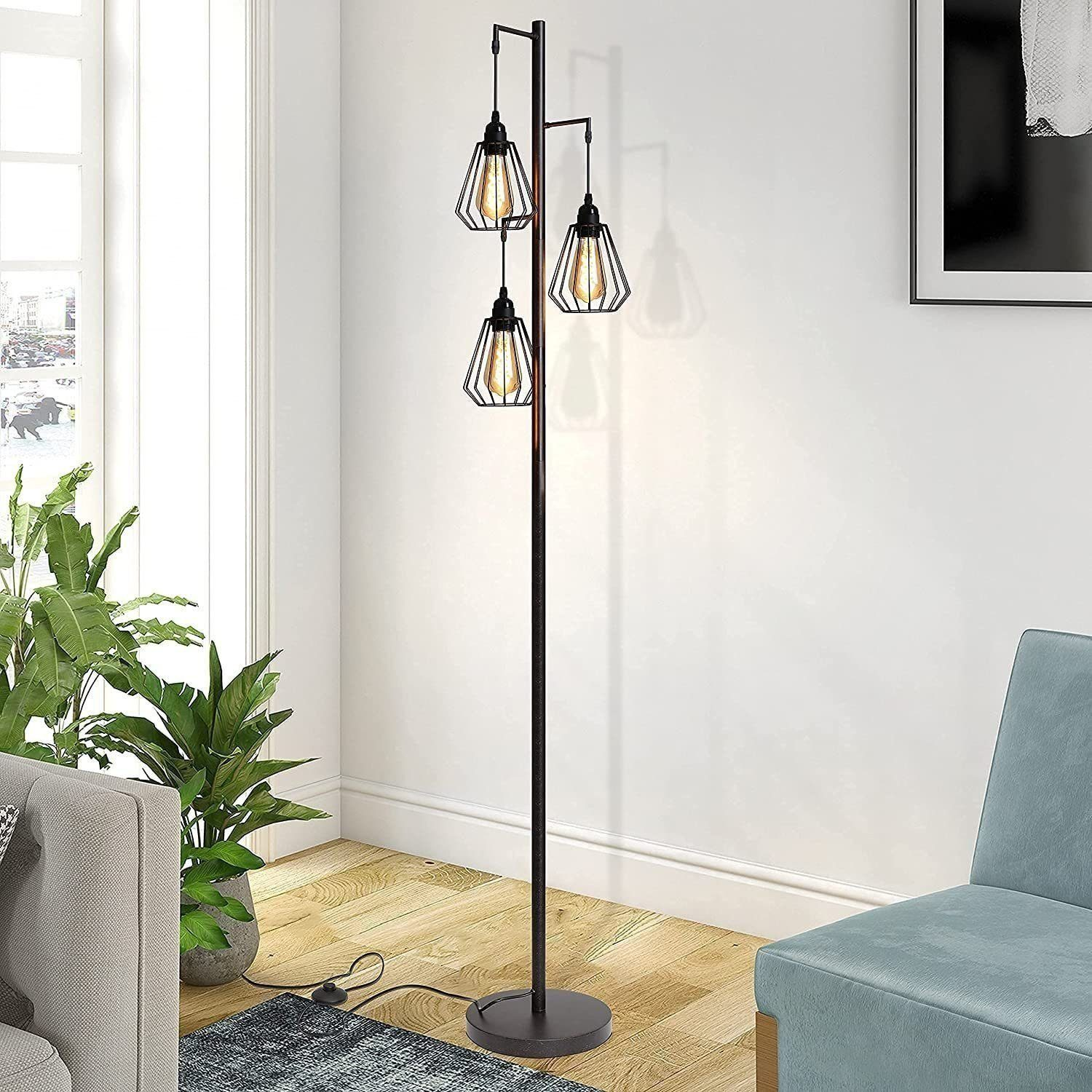 Lampada da terra nera alta con tre luci a gabbia geometriche sospese. Una finestra, piante e una sedia blu sullo sfondo.
