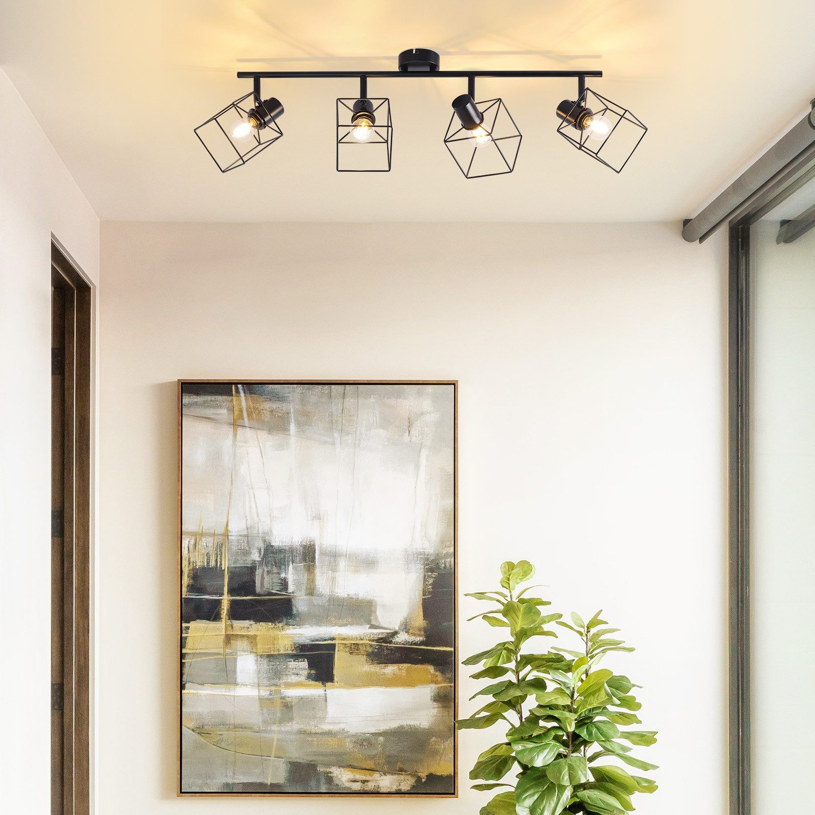 Quattro faretti neri su un soffitto. Sotto c'è un dipinto e una pianta verde.