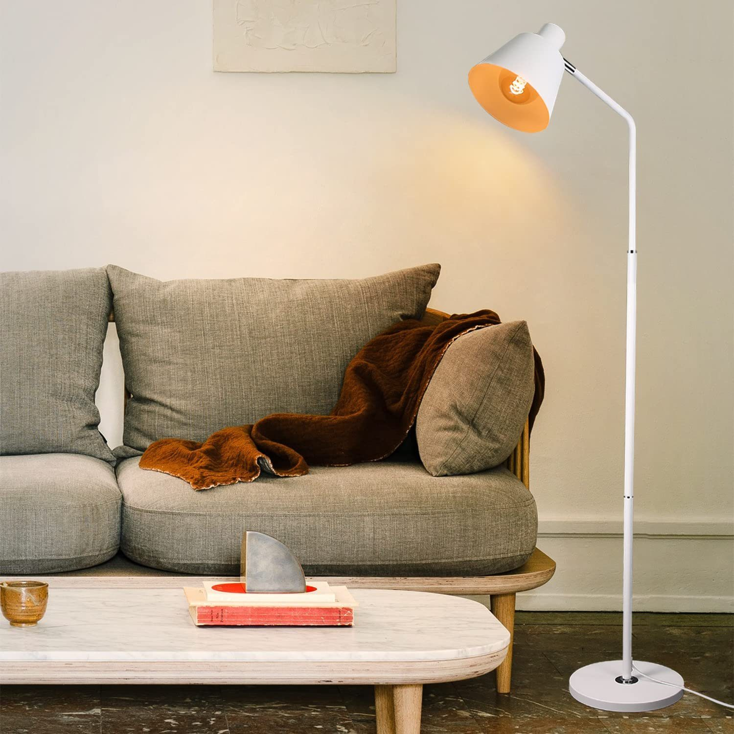 Eine weiße Stehlampe mit gebogenem Arm und weißem Lampenschirm. Es ist auf weißem Hintergrund.