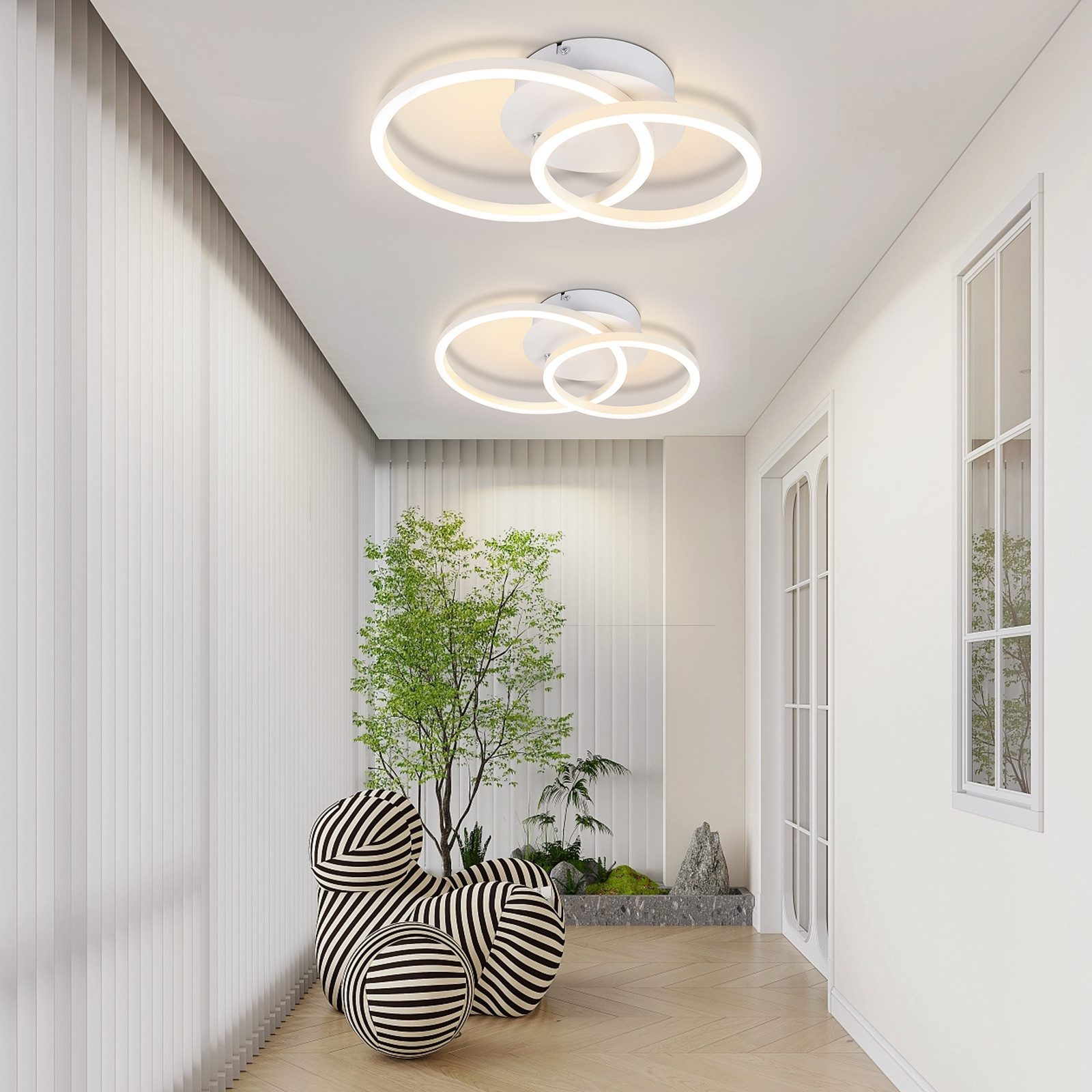 Un corridoio con pareti bianche, due luci a soffitto circolari, una pianta verde e sfere a strisce.