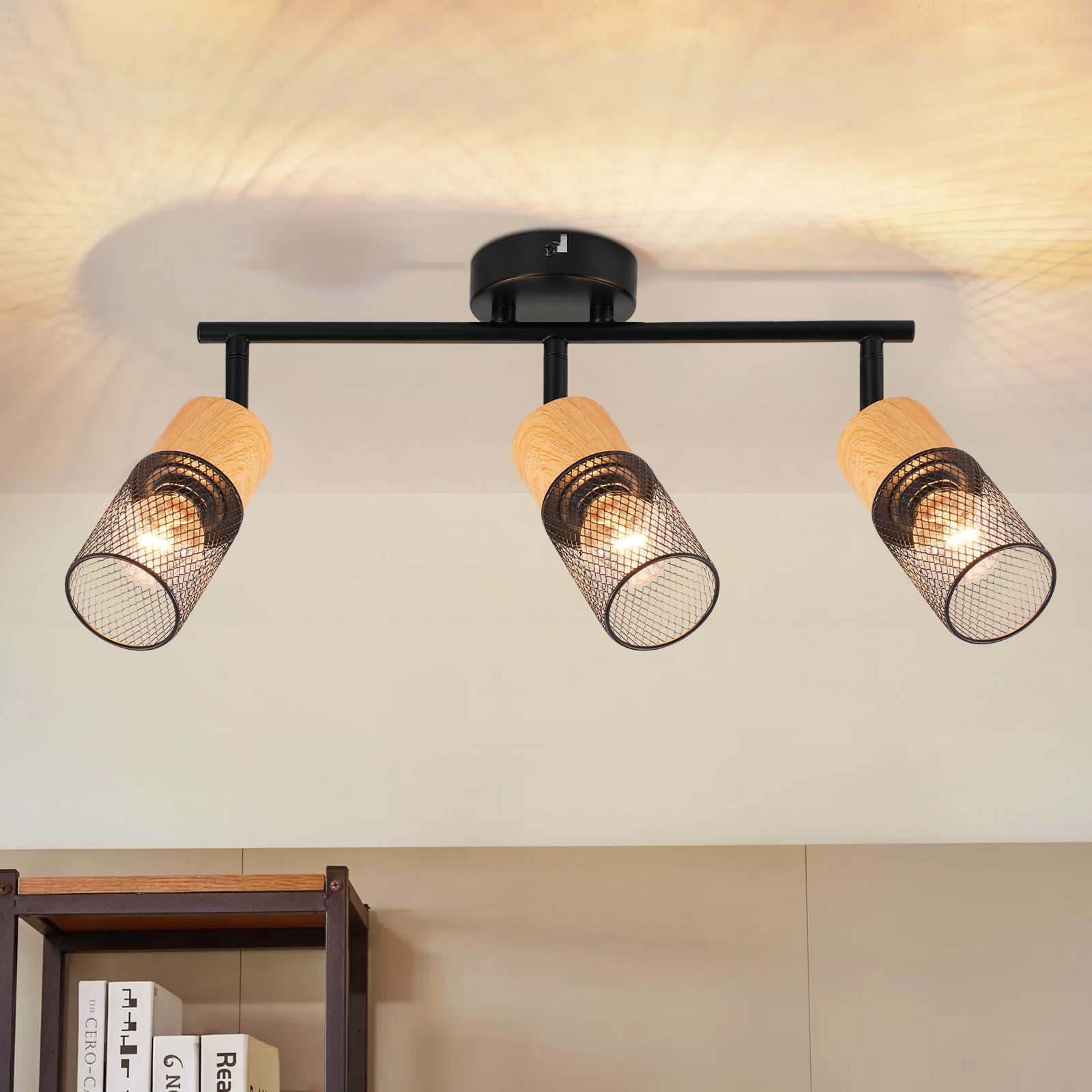 Oświetlenie sufitowe z trzema reflektorami, każdy z metalowym kloszem z siatki, zamontowane na czarnym drążku, z drewnianym akcentem.