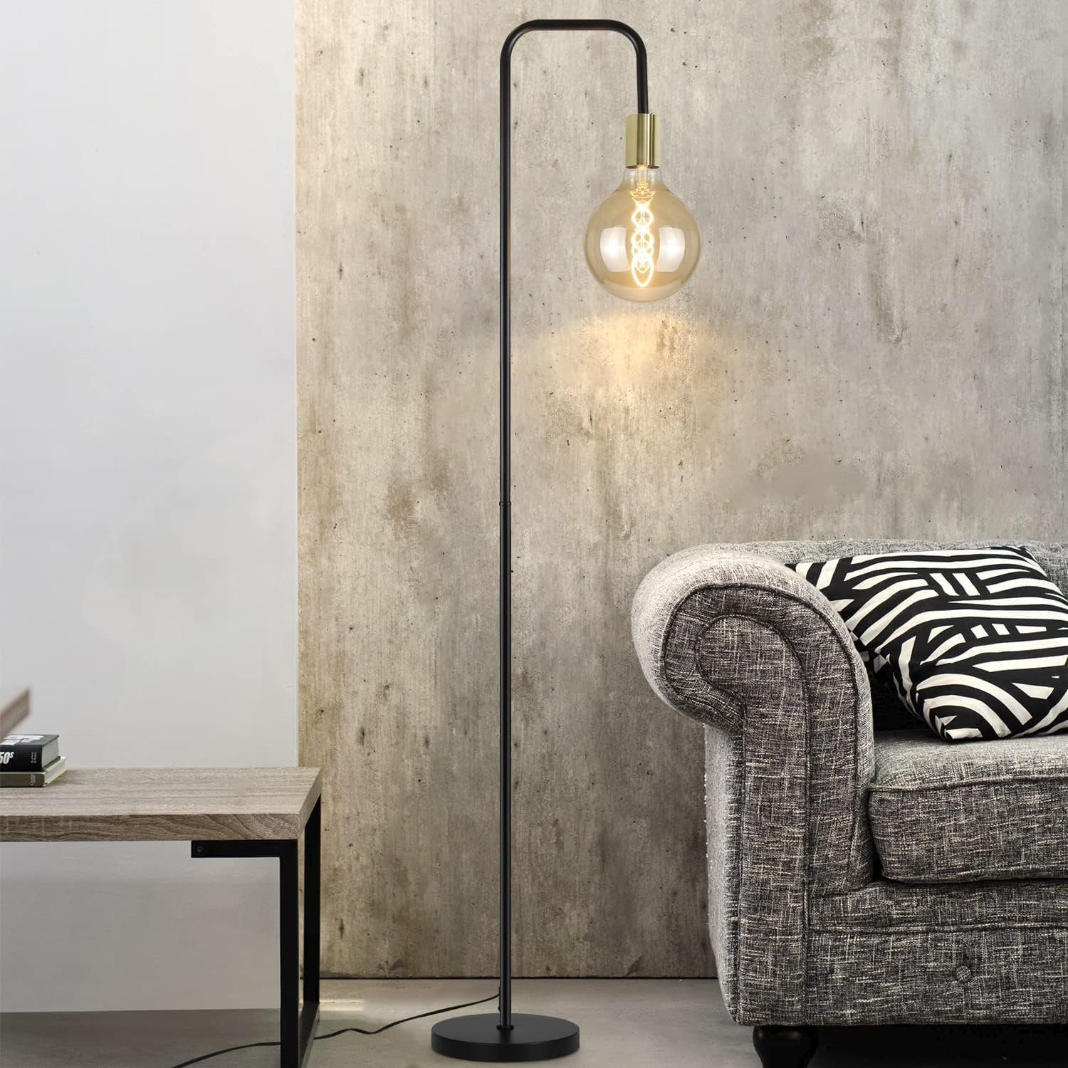 Lampada da terra nera con una lampadina dorata. La lampada è accanto a un divano grigio. Un tavolo di legno è accanto.