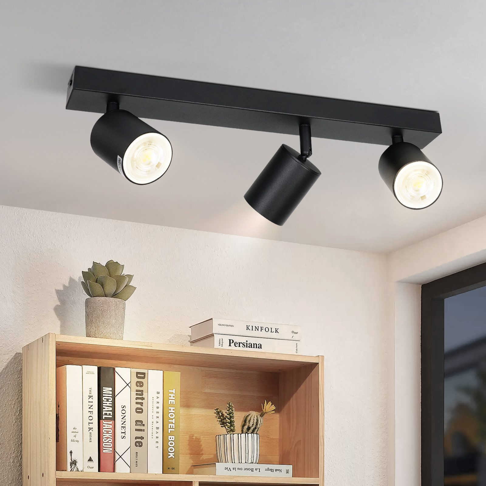 Czarna lampa sufitowa z trzema reflektorami, oświetlająca obszar nad drewnianą półką.