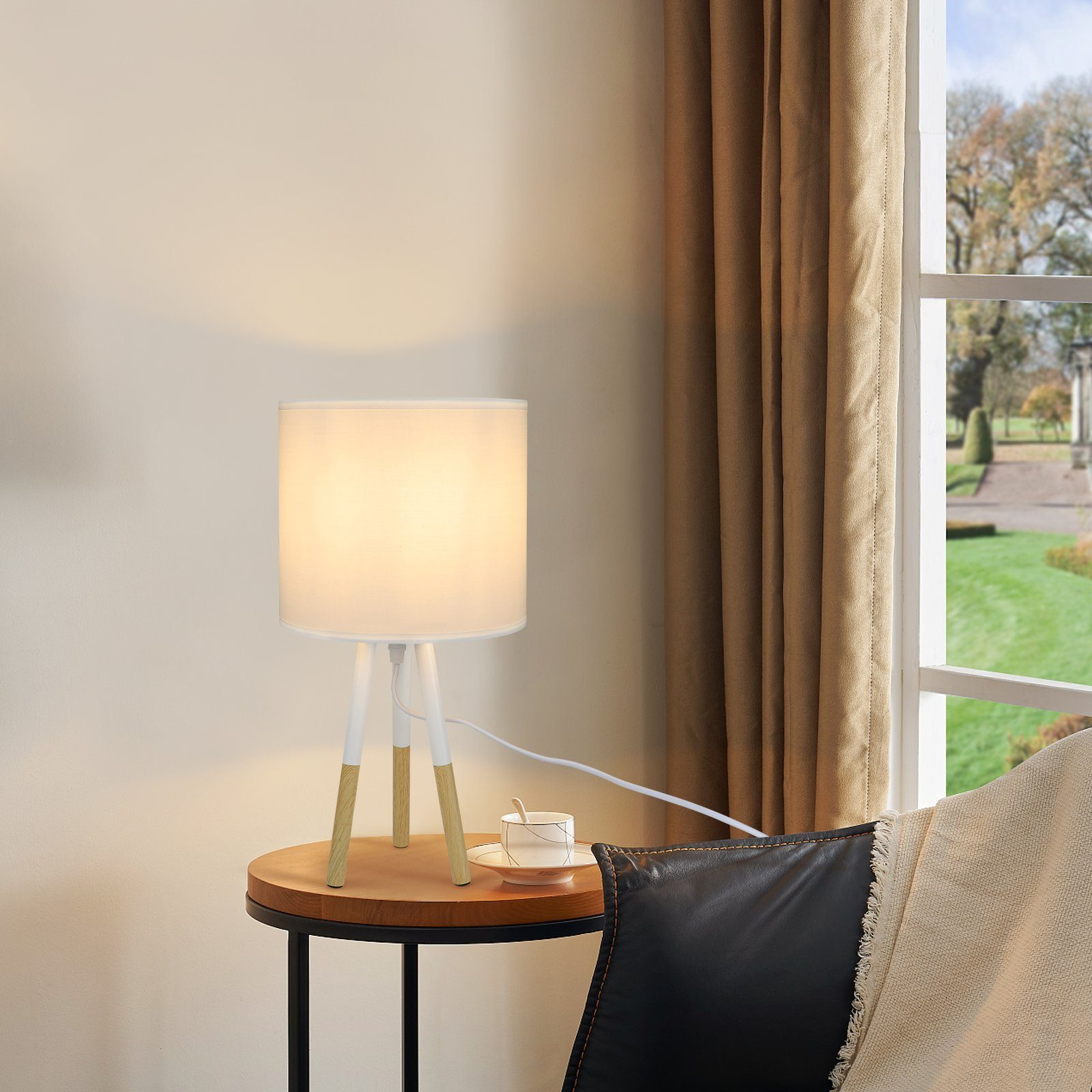 Biało-drewniana lampa stołowa na okrągłym stoliku z filiżanką kawy. Okno w tle.