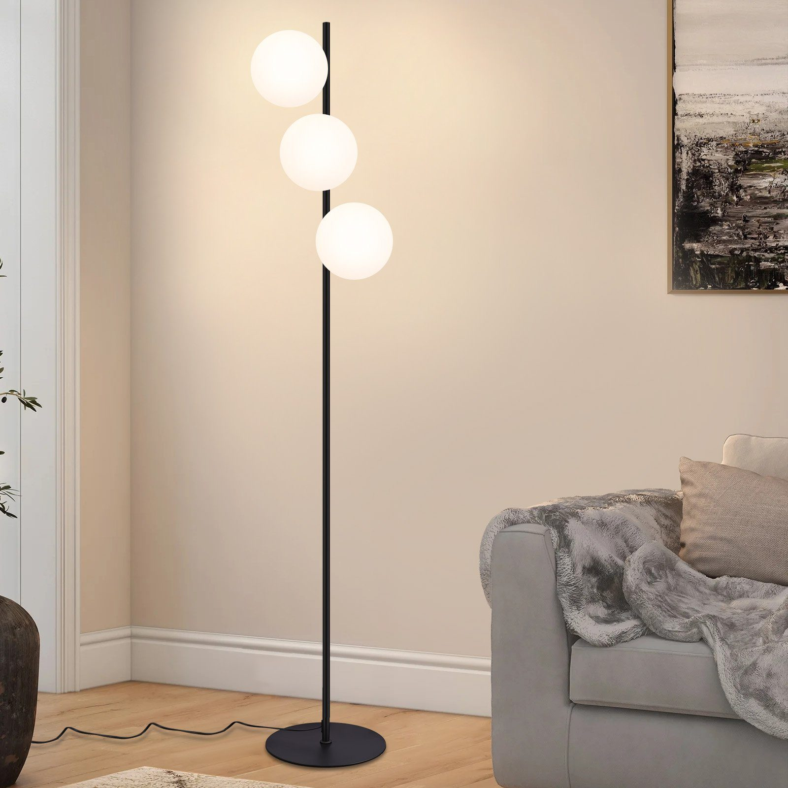 Lampada da terra con tre globi bianchi su un palo nero. Divano grigio e un dipinto sullo sfondo.