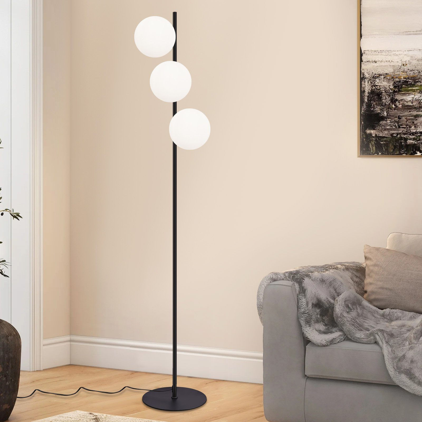 Una lampada da terra nera alta con tre globi bianchi, accanto a un divano.
