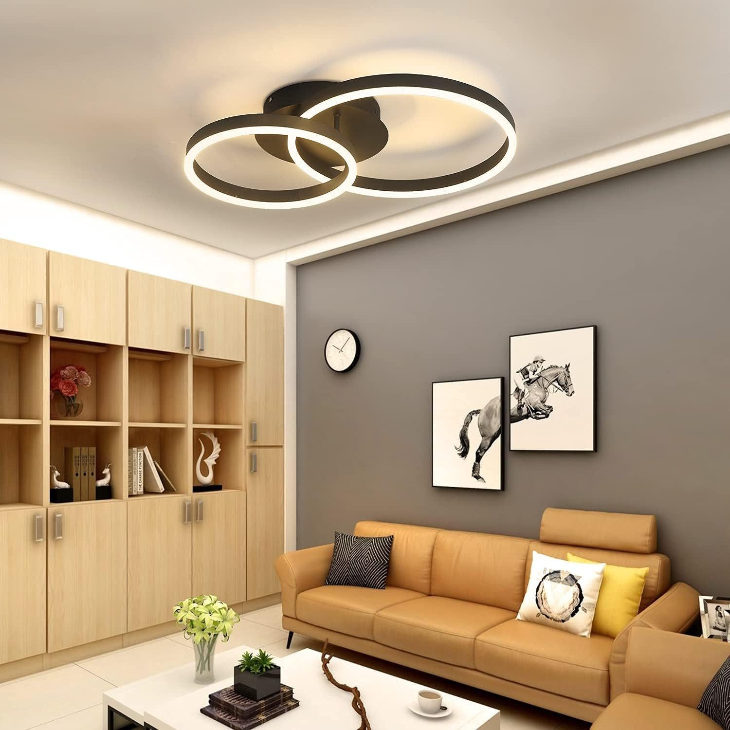 Soggiorno con due luci ad anello sul soffitto. Divano beige, quadri sul muro. Muro grigio.