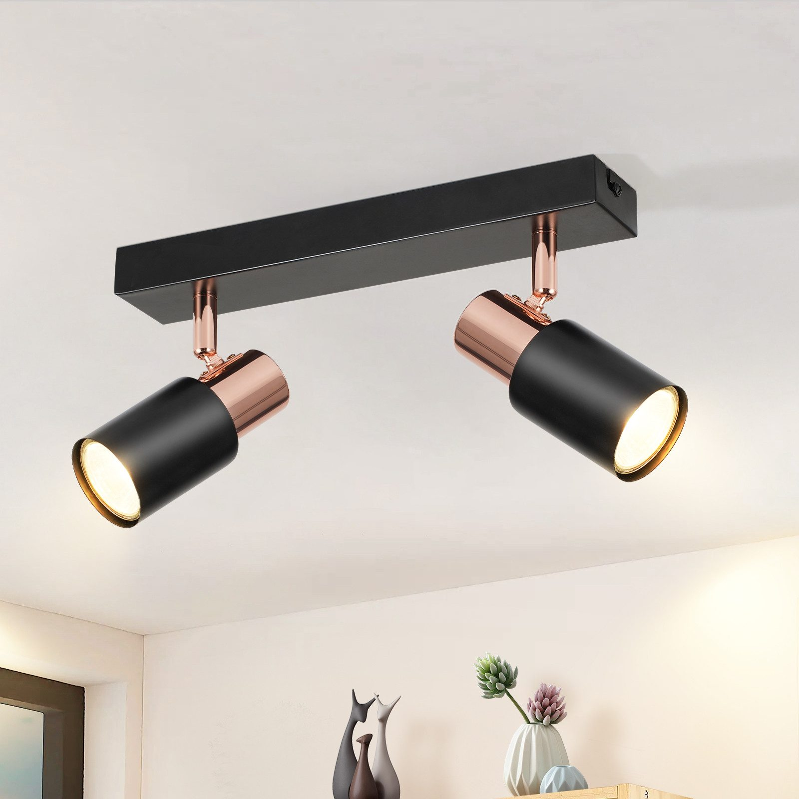 Due faretti neri con accenti ramati su un soffitto bianco. Le luci sono accese e illuminano.