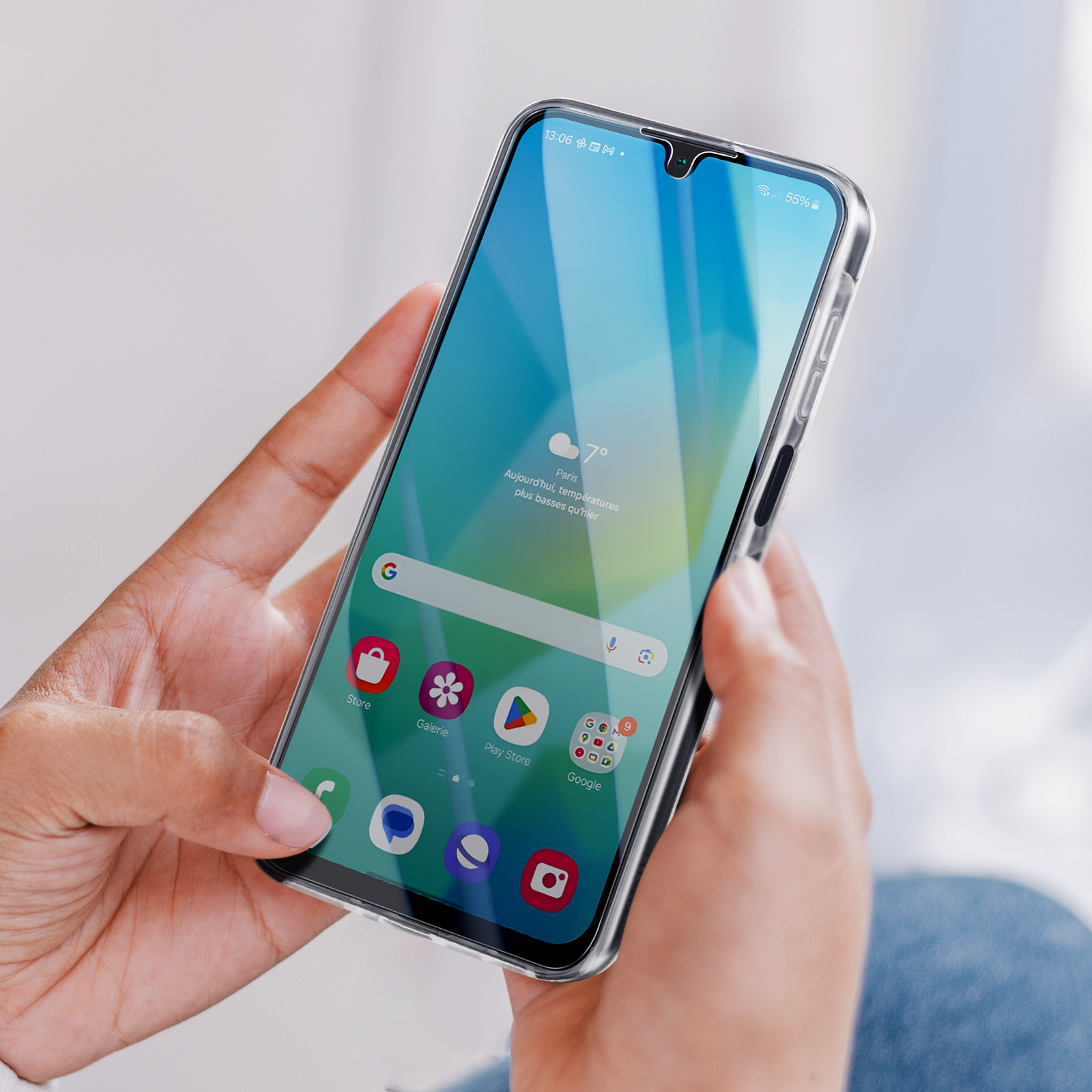 Le mani di una persona che tiene un telefono con una custodia trasparente, che mostra uno schermo blu e verde.