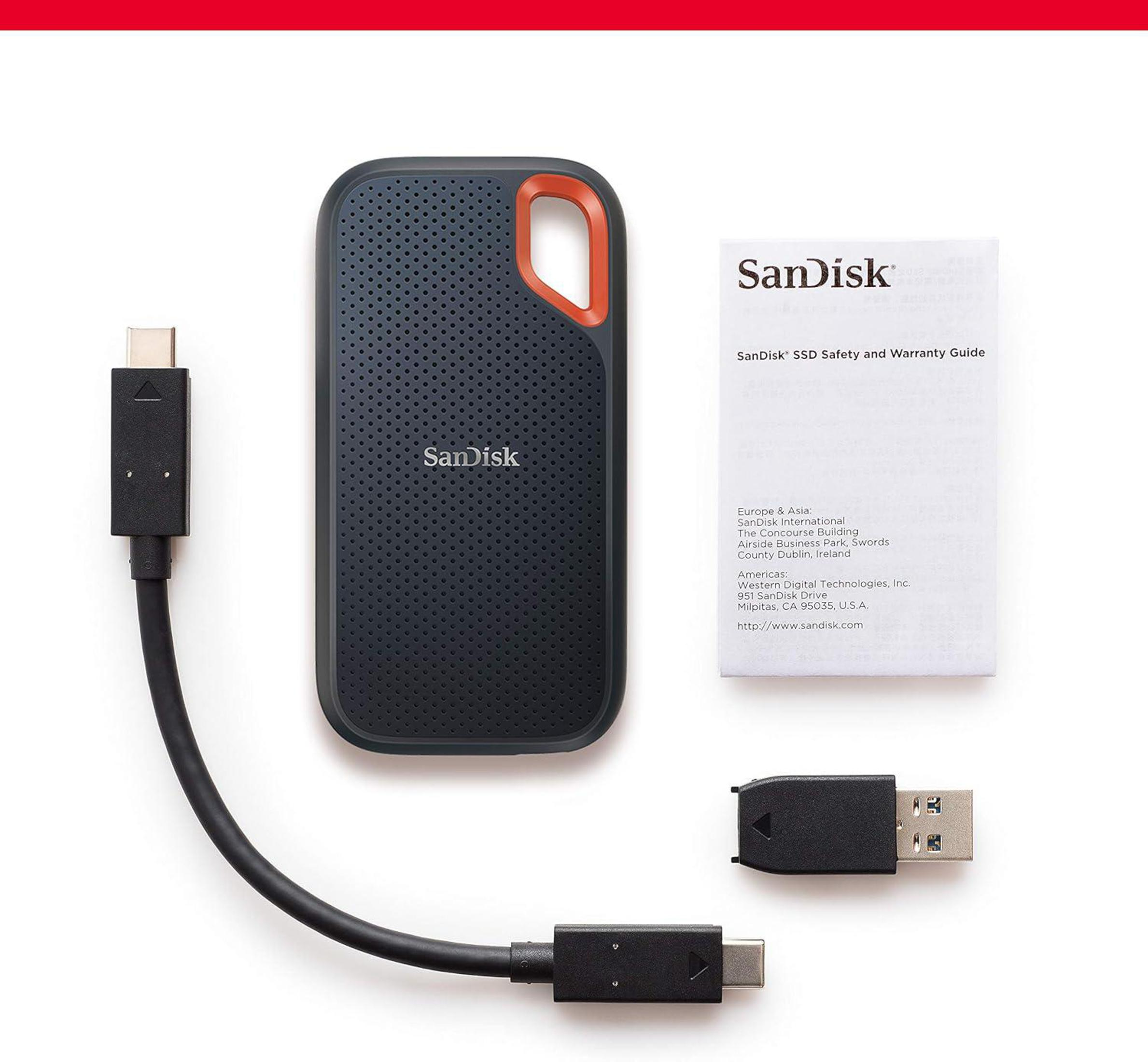 Czarny dysk SSD SanDisk, pomarańczowy uchwyt, kable i gwarancja na białej powierzchni.