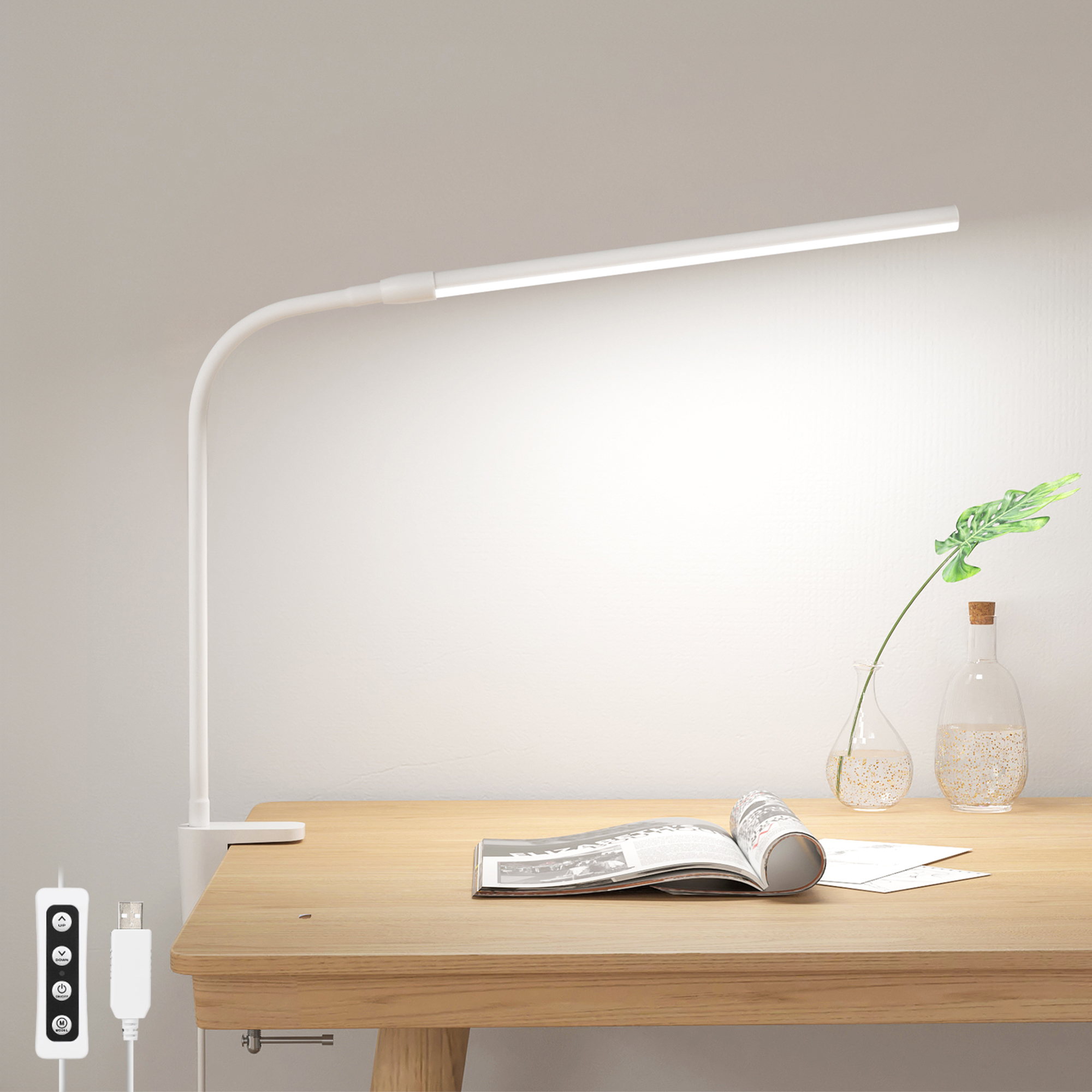 Weiße Schreibtischlampe mit flexiblem Hals, neben einem Schreibtisch mit Buch und Pflanzen.