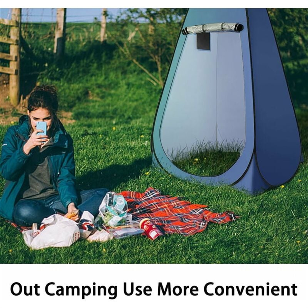 Eine Frau benutzt ein Handy, während sie auf dem Gras neben einem blauen Pop-up-Zelt mit einer roten Decke sitzt.