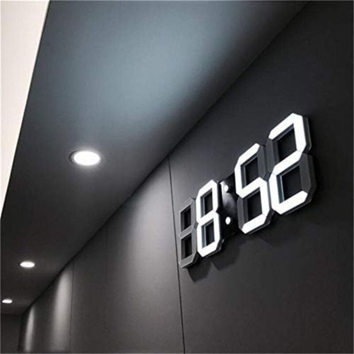 Digitaluhr mit der Anzeige 08:52, montiert an einer dunkelgrauen Wand mit Strahlern.
