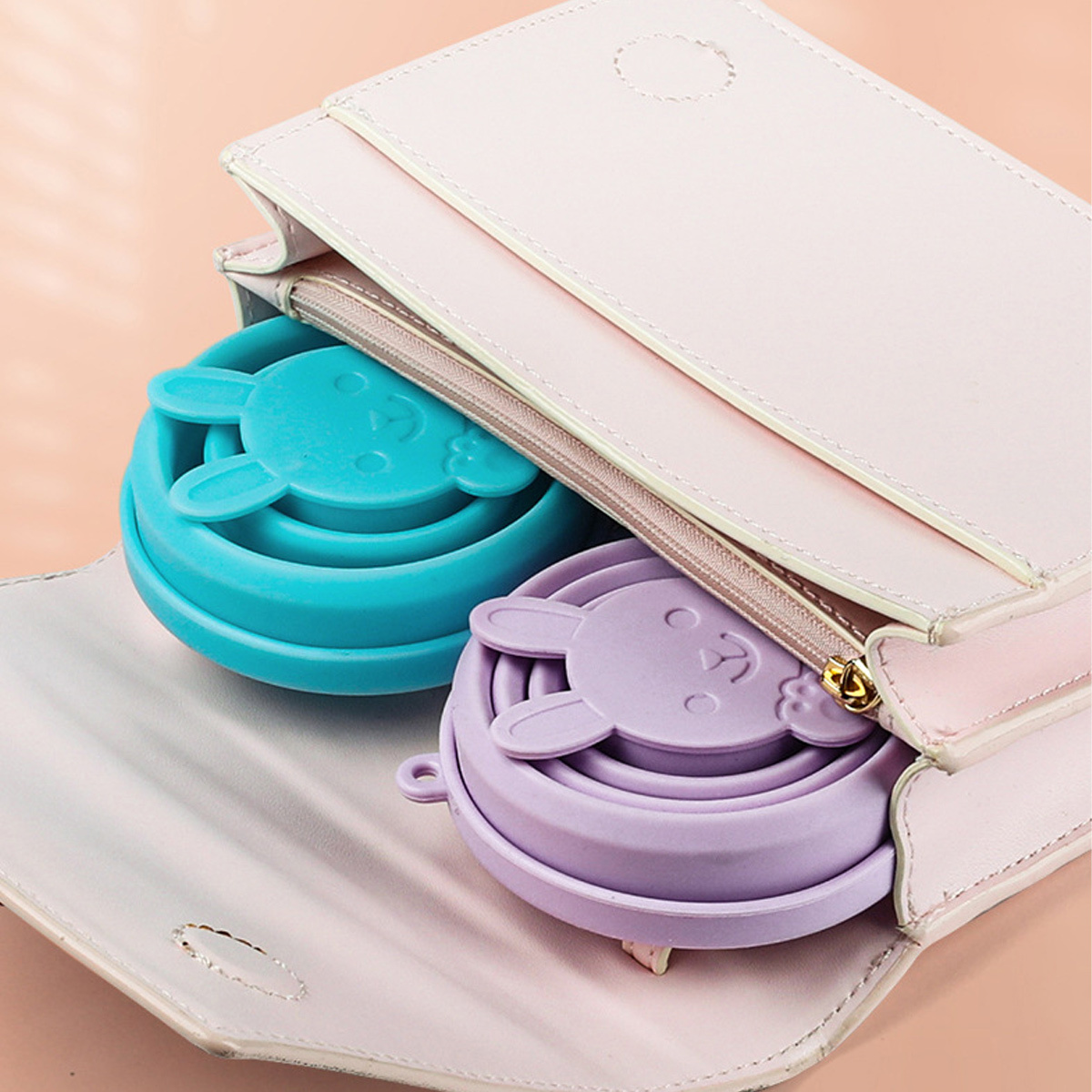 Zwei zusammenklappbare Silikonbecher in einer rosa Handtasche. Ein Becher ist blau, der andere lila.