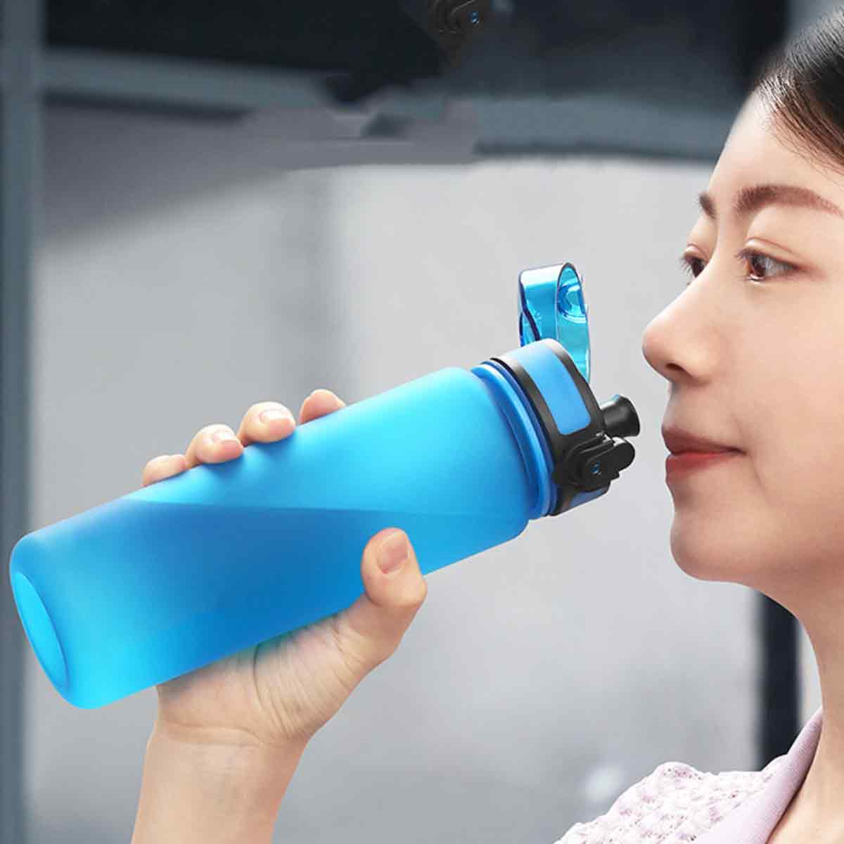 Eine Frau trinkt aus einer blauen Wasserflasche, die sie in der Hand hält.