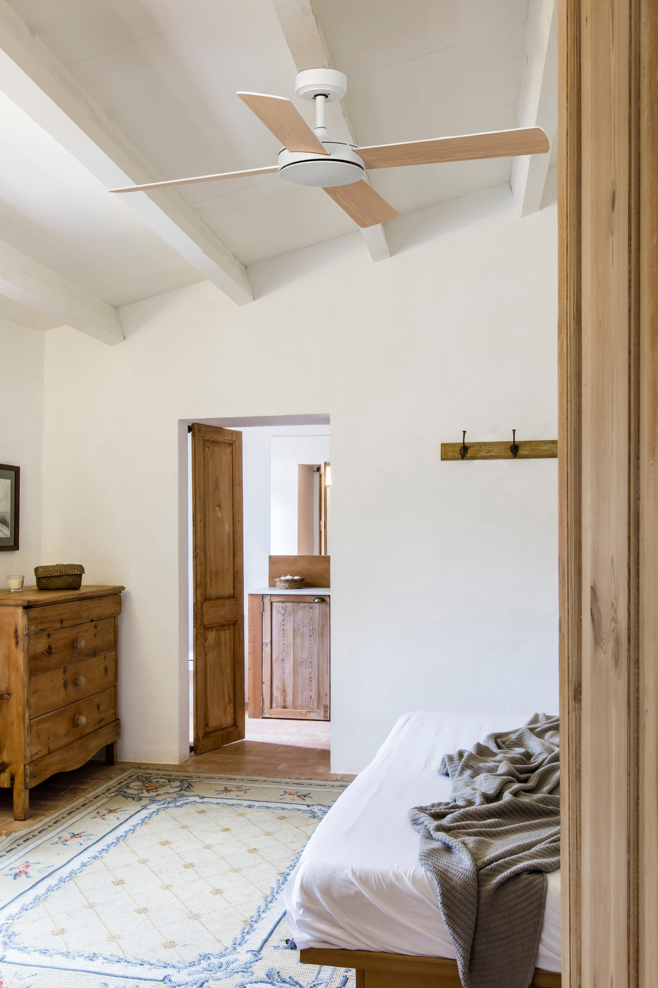 Helles Schlafzimmer mit Deckenventilator, Bett, Kommode und Tür zu einem anderen Raum.