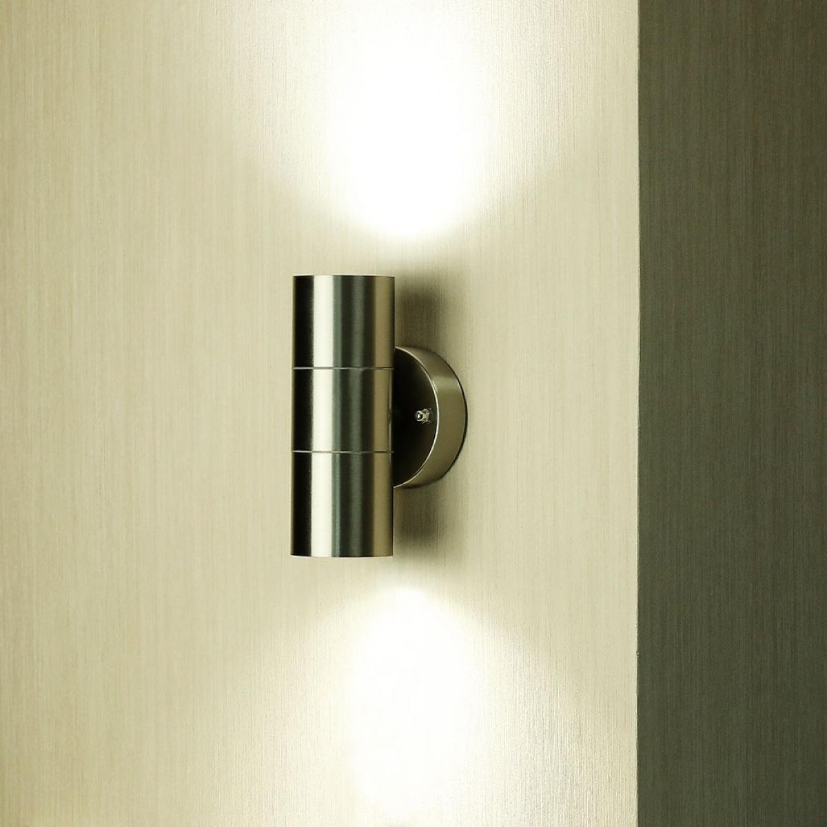 Silberne zylindrische Lampe an einer beigen Wand montiert.
