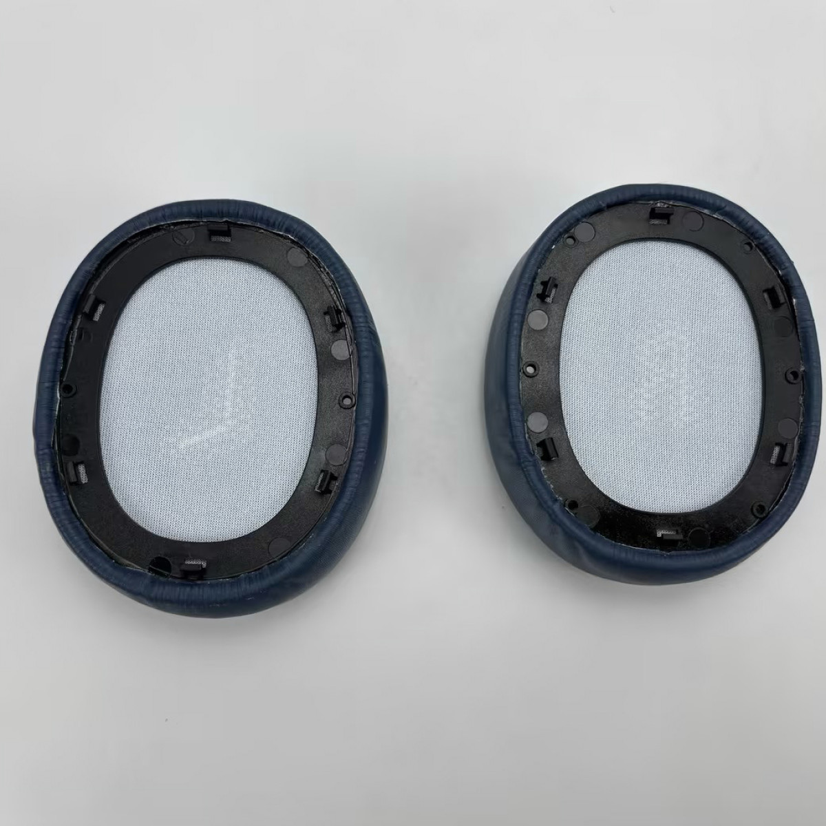 Dwie niebiesko-czarne wkładki do uszu, z jasnoniebieską siateczką wewnątrz i czarną ramką.