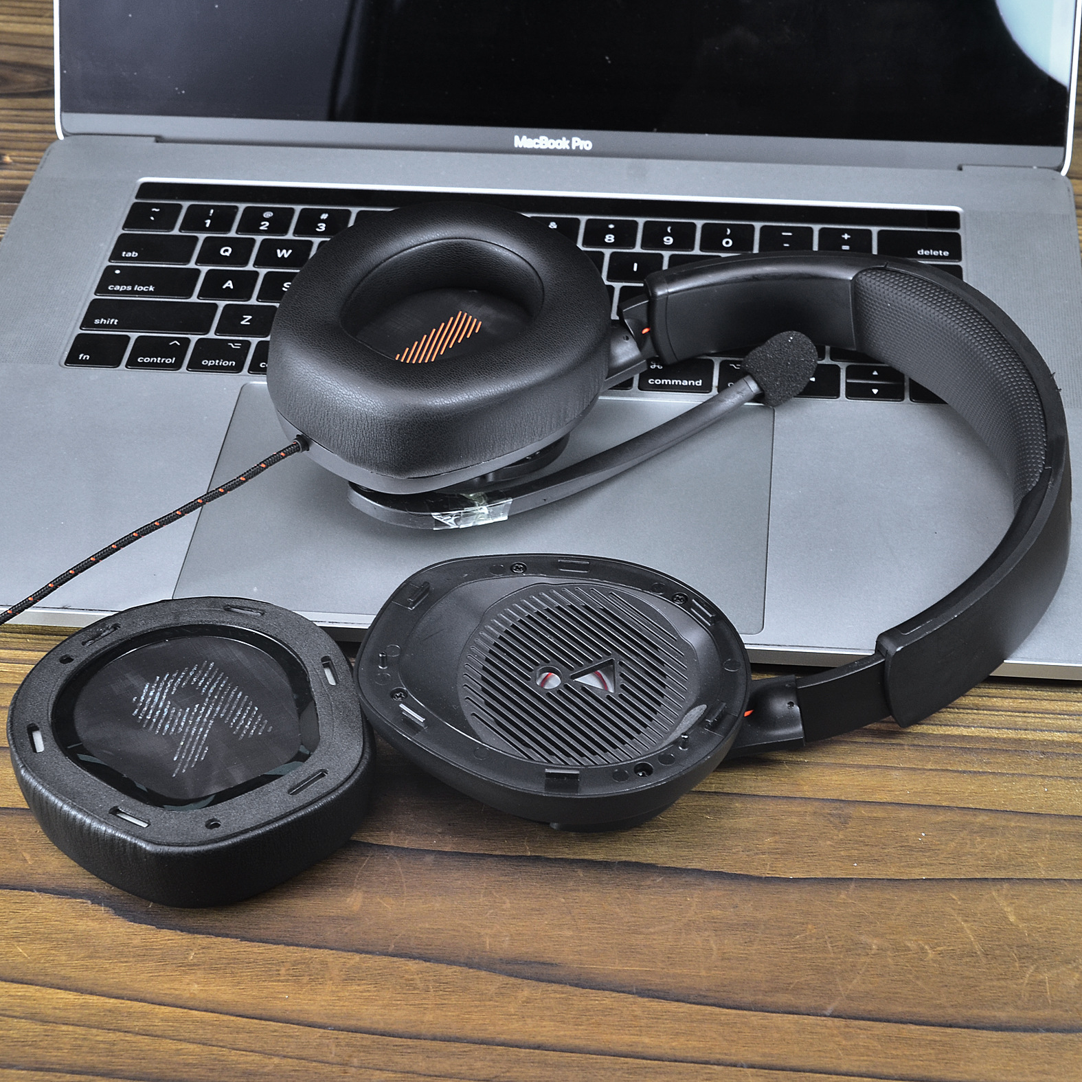 Czarne słuchawki zdemontowane na laptopie, pokazujące nauszniki i elementy wewnętrzne, na drewnianym stole.