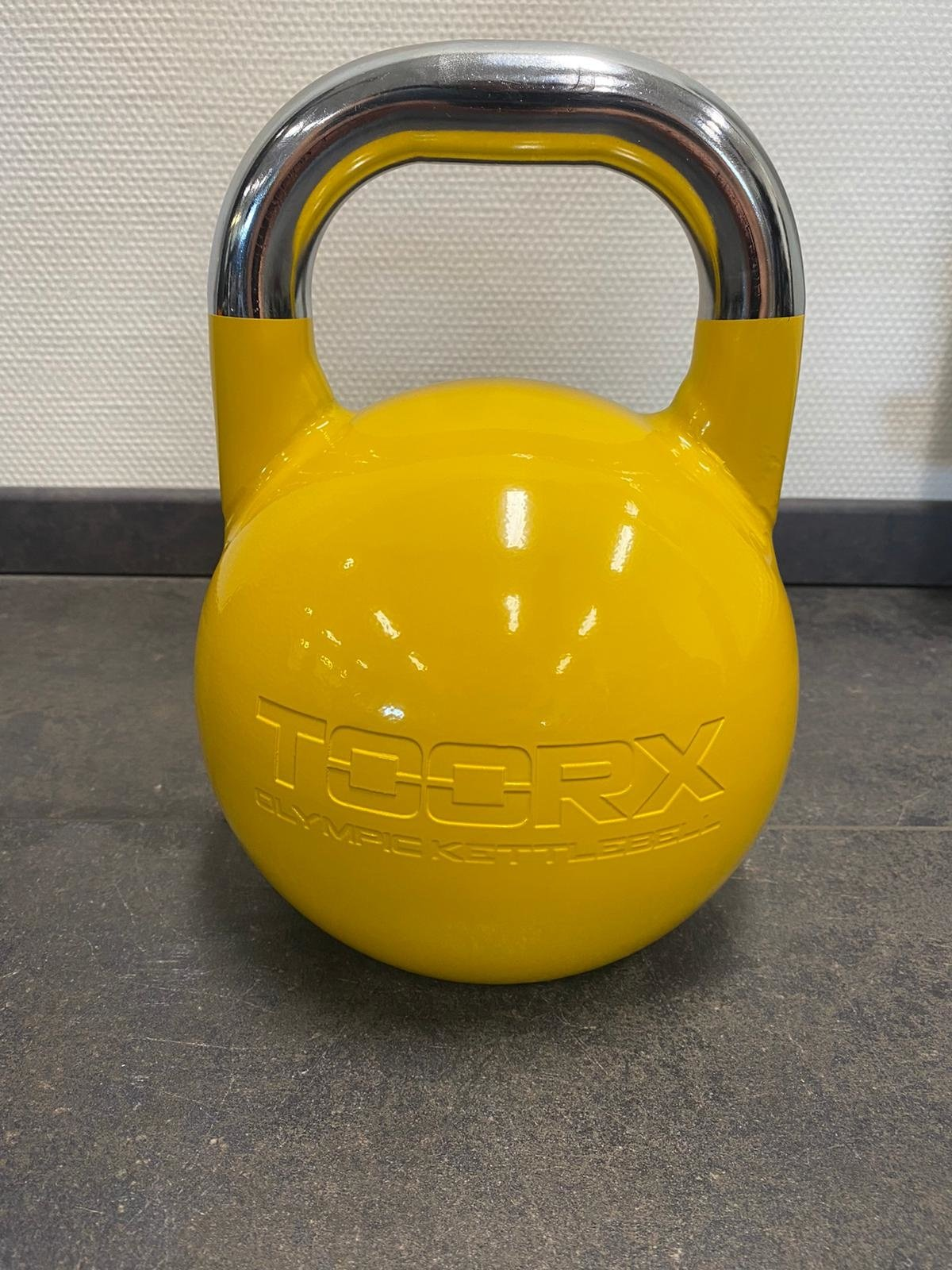 Gelbe Kettlebell auf grauem Boden. Der Griff ist silberfarben.