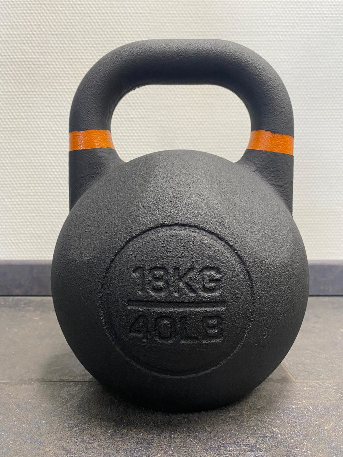 Schwarze Kettlebell mit orangefarbenen Akzenten am Griff. Zeigt '18KG 40LB'.