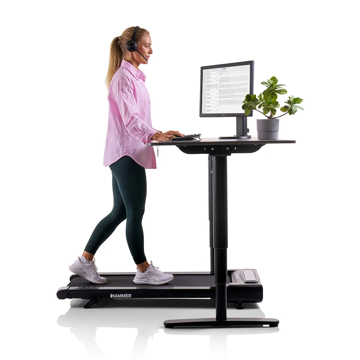 Frau geht auf einem Laufband-Schreibtisch, trägt ein Headset und arbeitet am Computer.