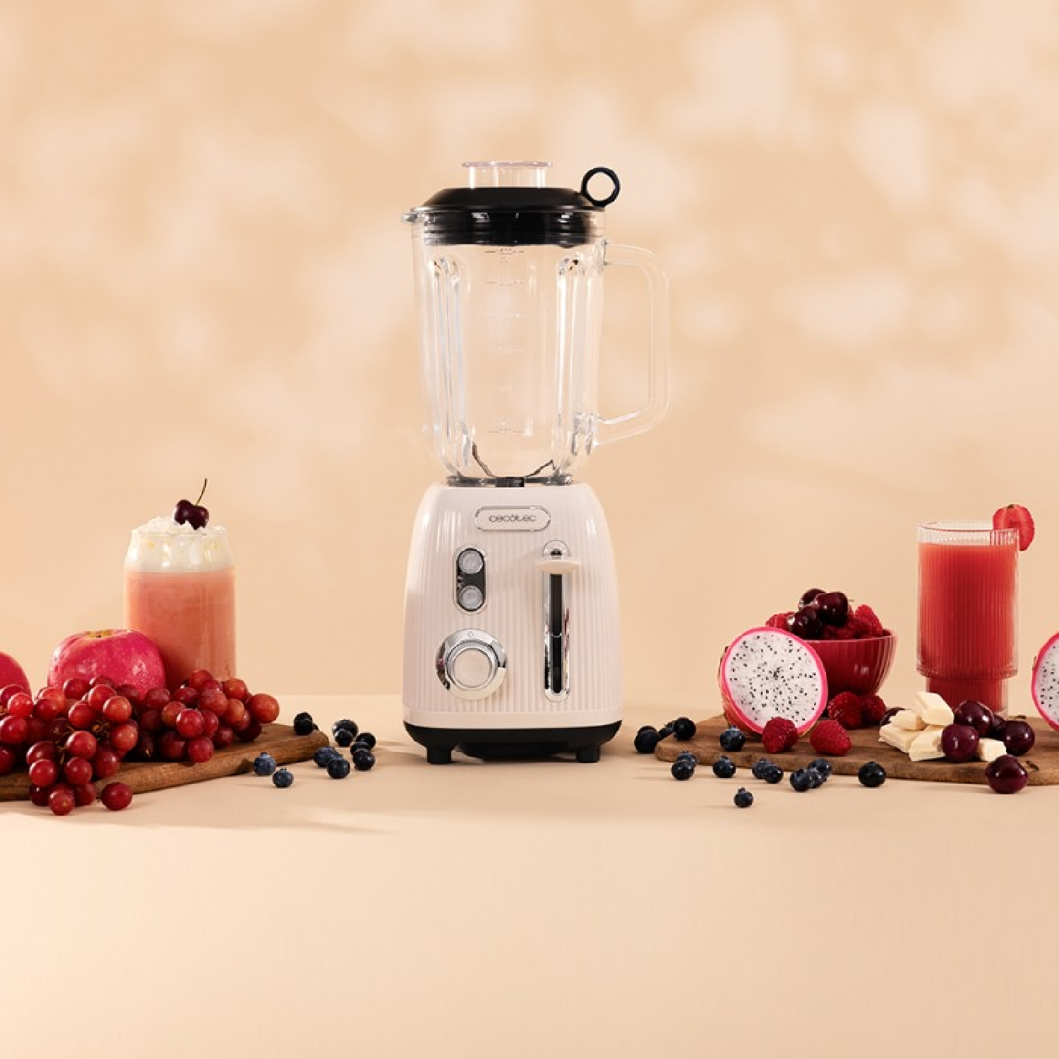 Un frullatore con frutta e bevande su una superficie beige. Include un frullatore, frutta e due bevande.