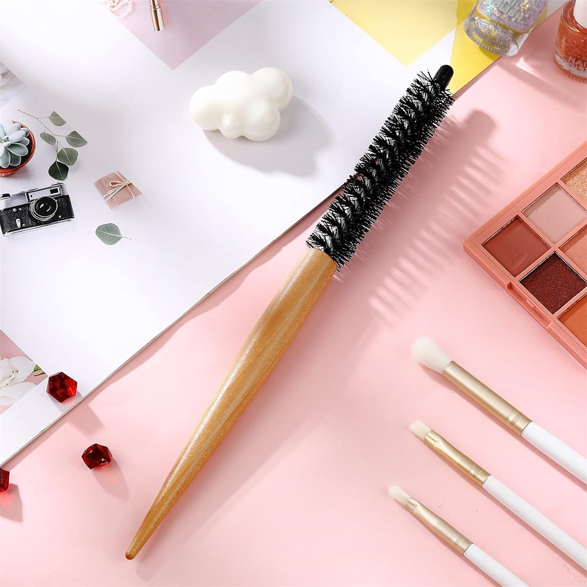 Runde Haarbürste mit Holzgriff und andere Make-up-Pinsel auf rosa Oberfläche.