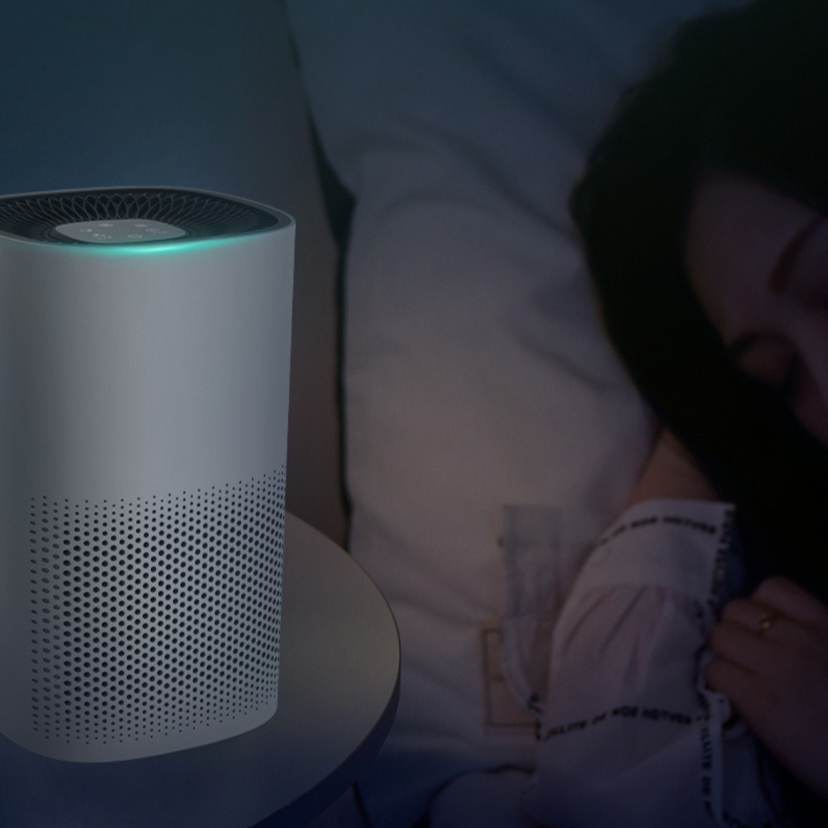 Luftreiniger auf einem Nachttisch, im Hintergrund eine schlafende Frau im Bett.