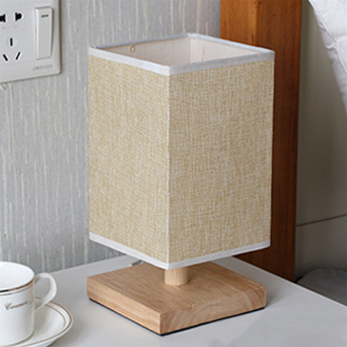 Quadratische beige Lampe auf Holzsockel auf weißem Tisch.