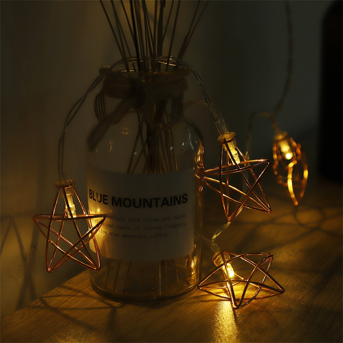 Lichterkette mit Sternformen in der Nähe einer Glasflasche mit Schriftzug; dunkler Hintergrund.