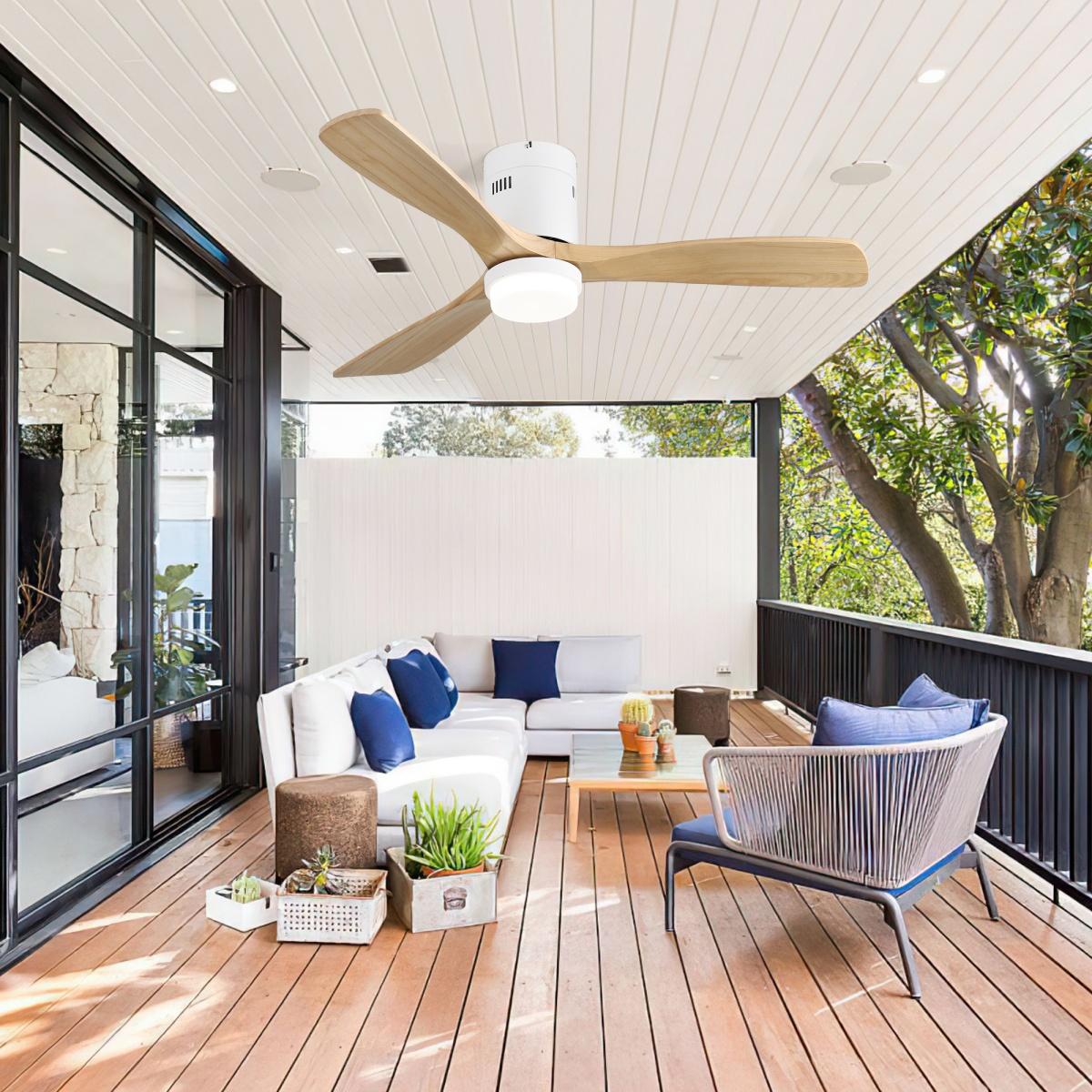 Terrasse im Freien mit weißem Sofa, Deckenventilator, Holzterrasse und blauen Kissen.