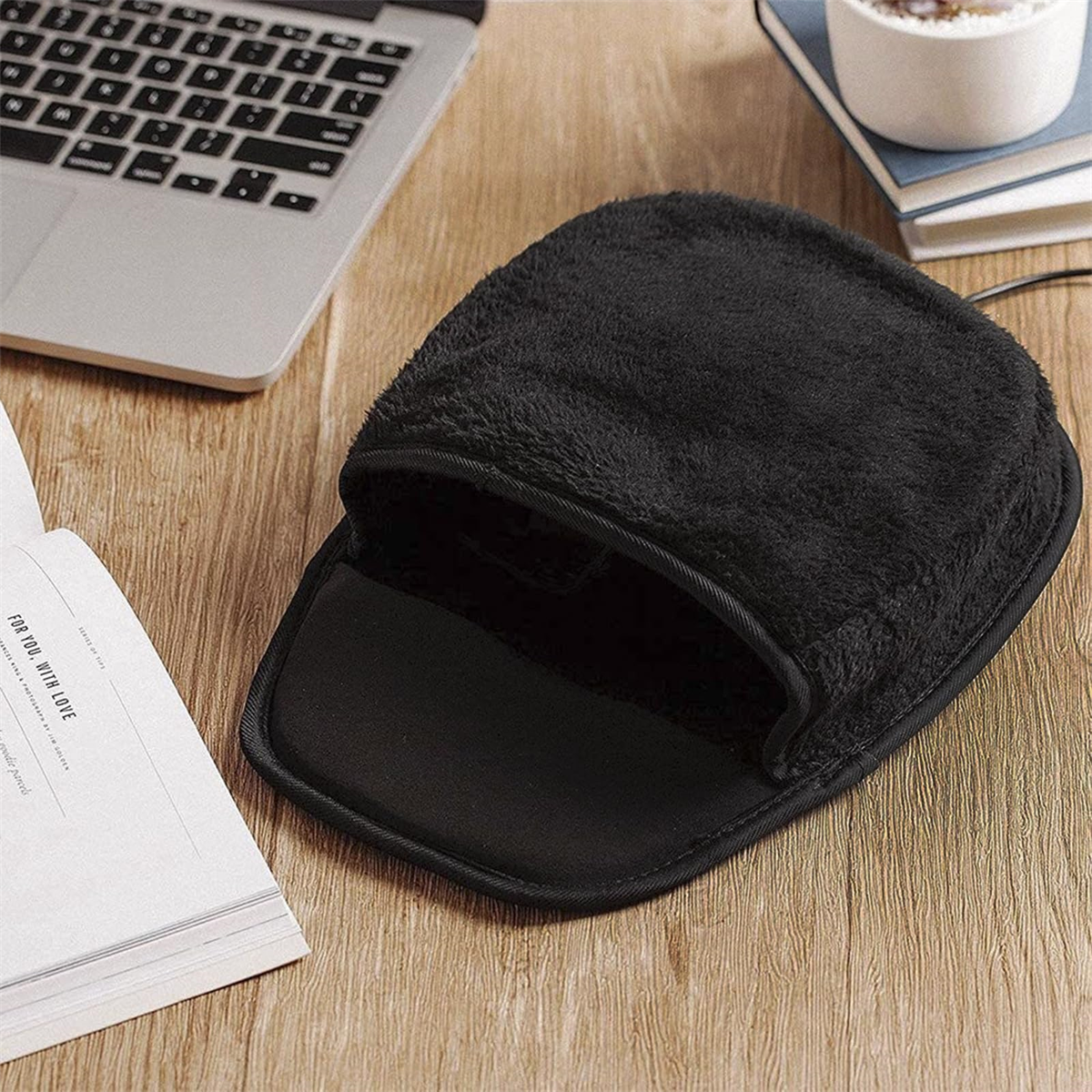 Ein schwarzes, beheiztes Mauspads auf einem Holztisch mit Laptop und Büchern im Blick.
