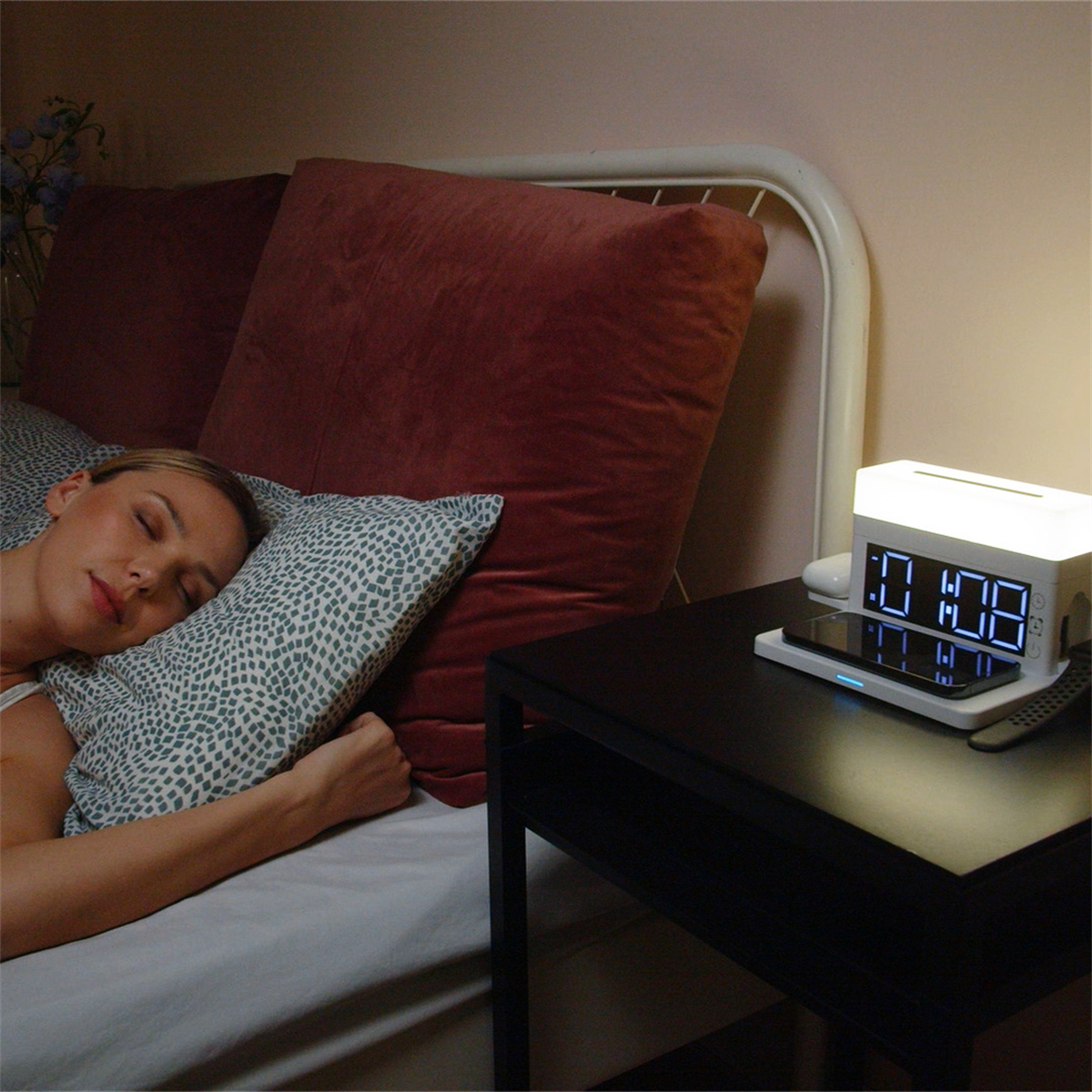 Eine Frau schläft im Bett mit einem Nachttisch-Wecker, der die Uhrzeit und ein Ladegerät anzeigt.