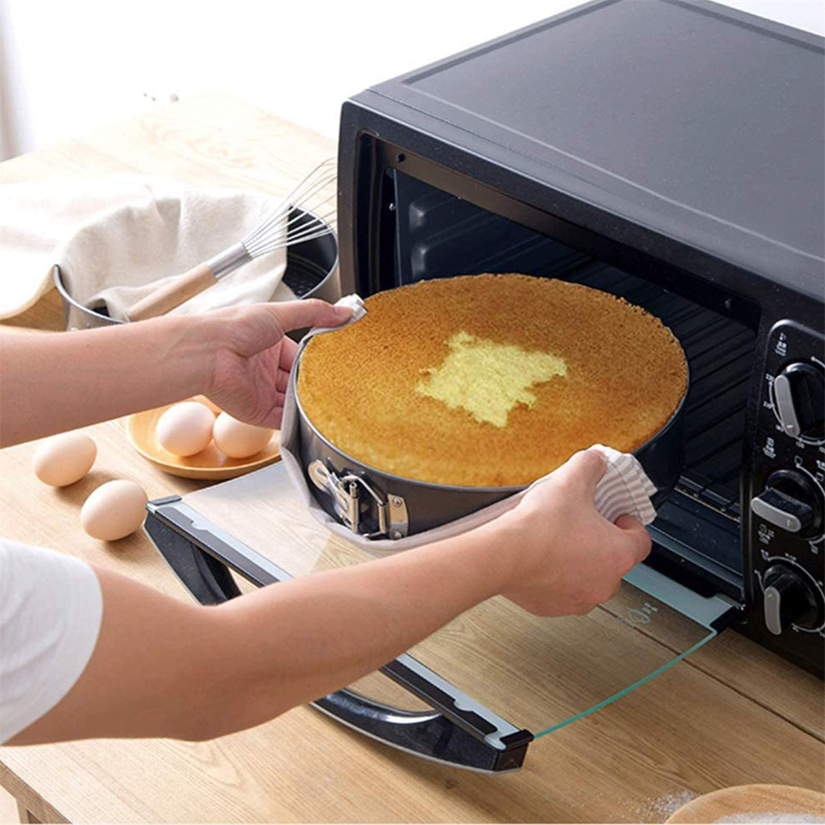 Ein Kuchen in einer Backform wird mit einem Tuch aus dem Ofen genommen, Eier im Hintergrund.