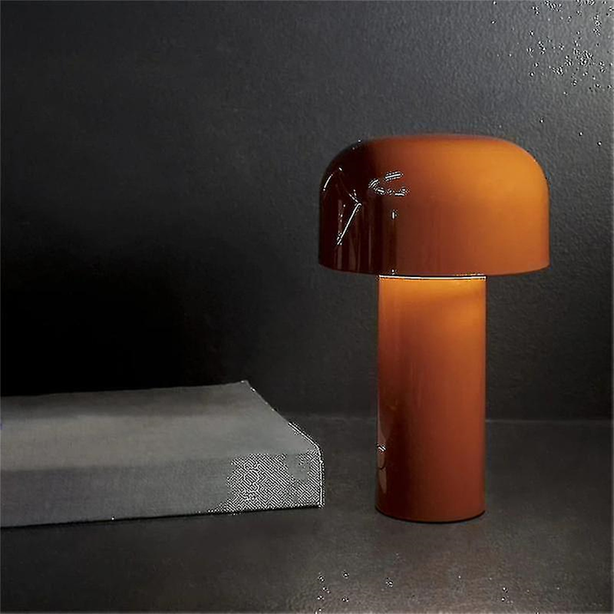 Orangefarbene Lampe mit rundem Oberteil und zylindrischem Sockel auf dunkler Oberfläche neben einem grauen Block.
